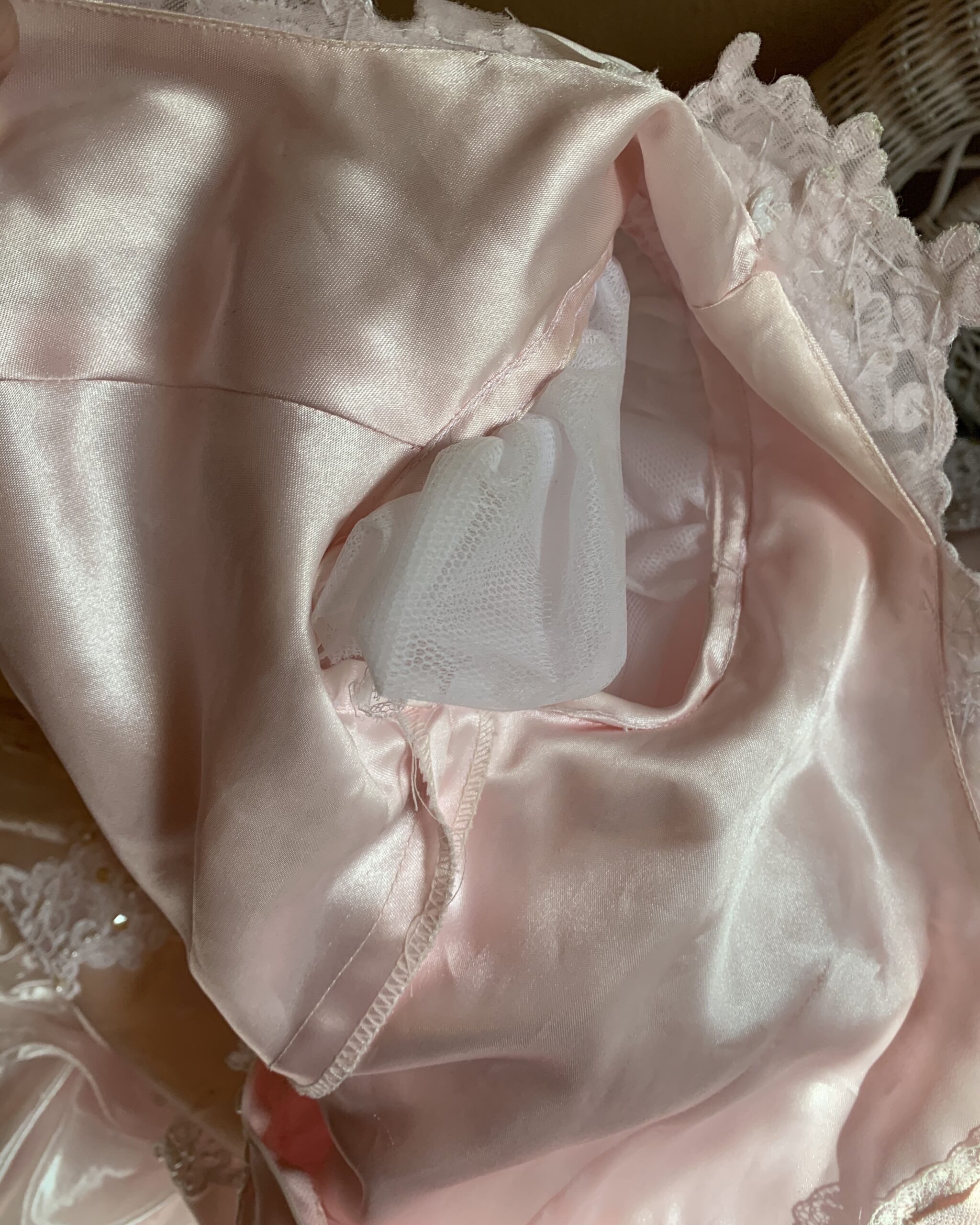 Interior construction detail of a vintage blush pink bridal gown showing satin lining, built-in tulle support layer, and layered skirt structure beneath the embellished lace bodice.