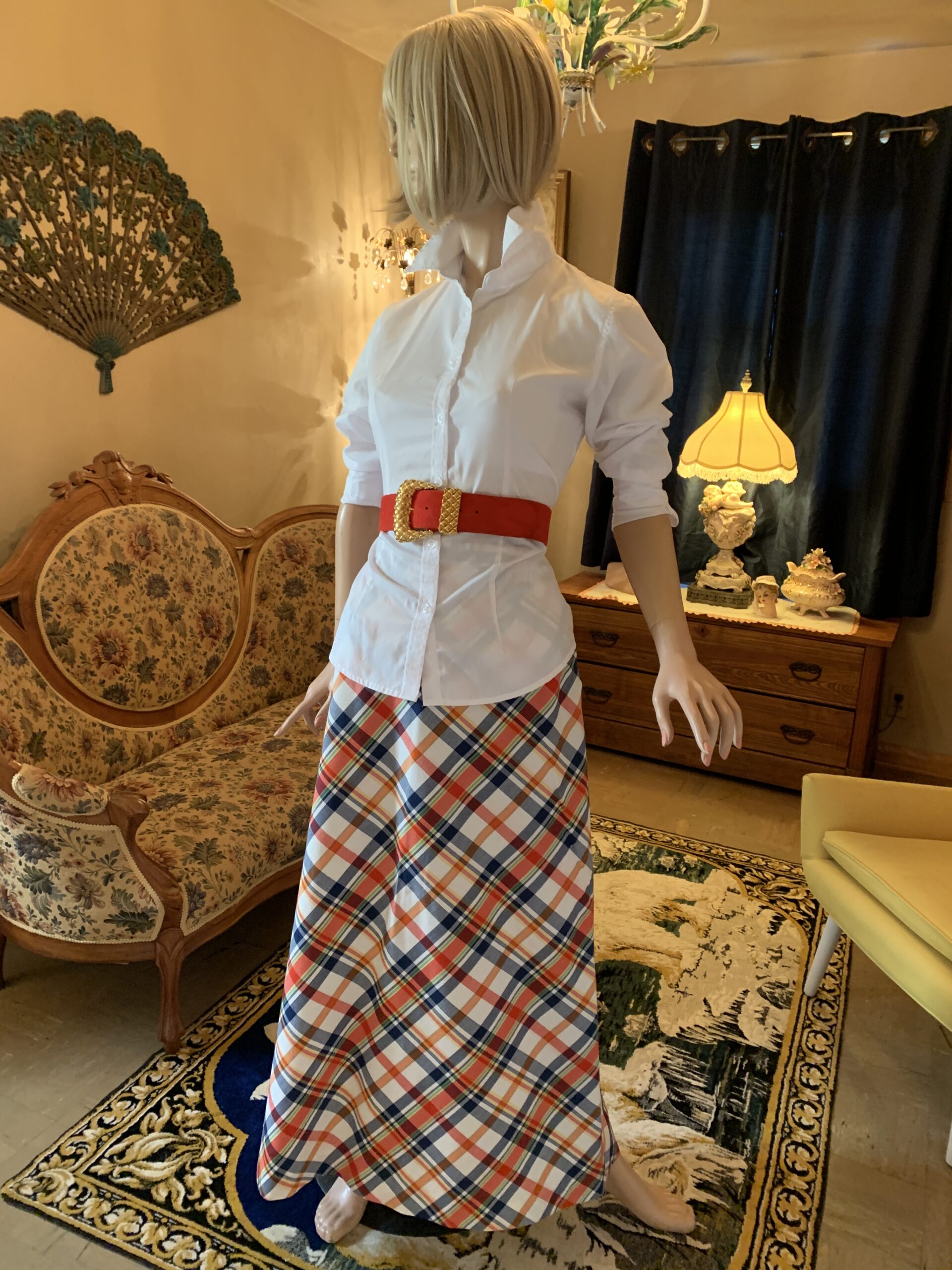 Vintage 1970s Prestige of Boston plaid A-line maxi skirt in red, navy, cream, and yellow plaid shown in salon setting.