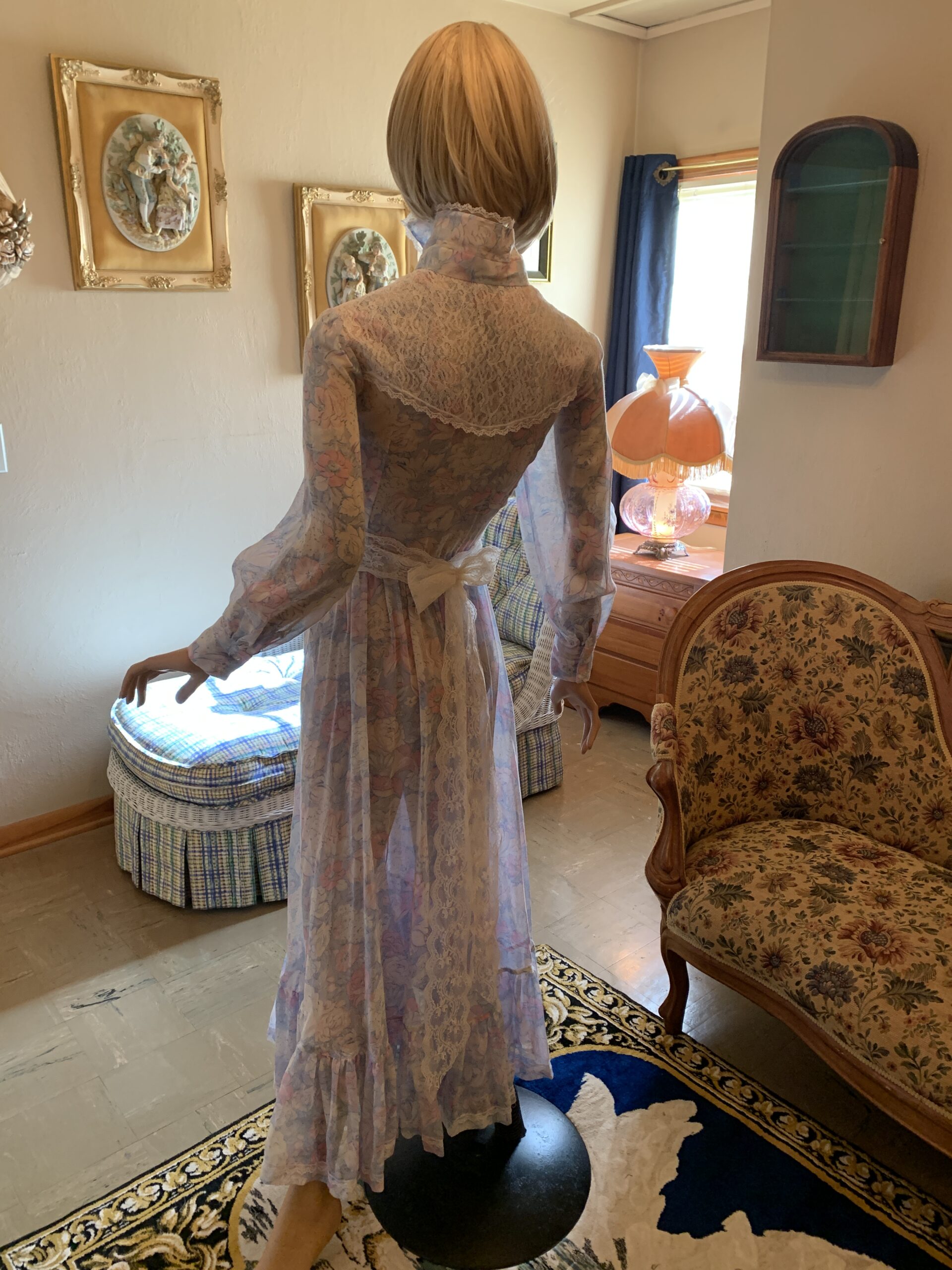 Back view of a 1970s floral voile dress showing lace yoke detail, long sleeves, gathered skirt, and attached sash.