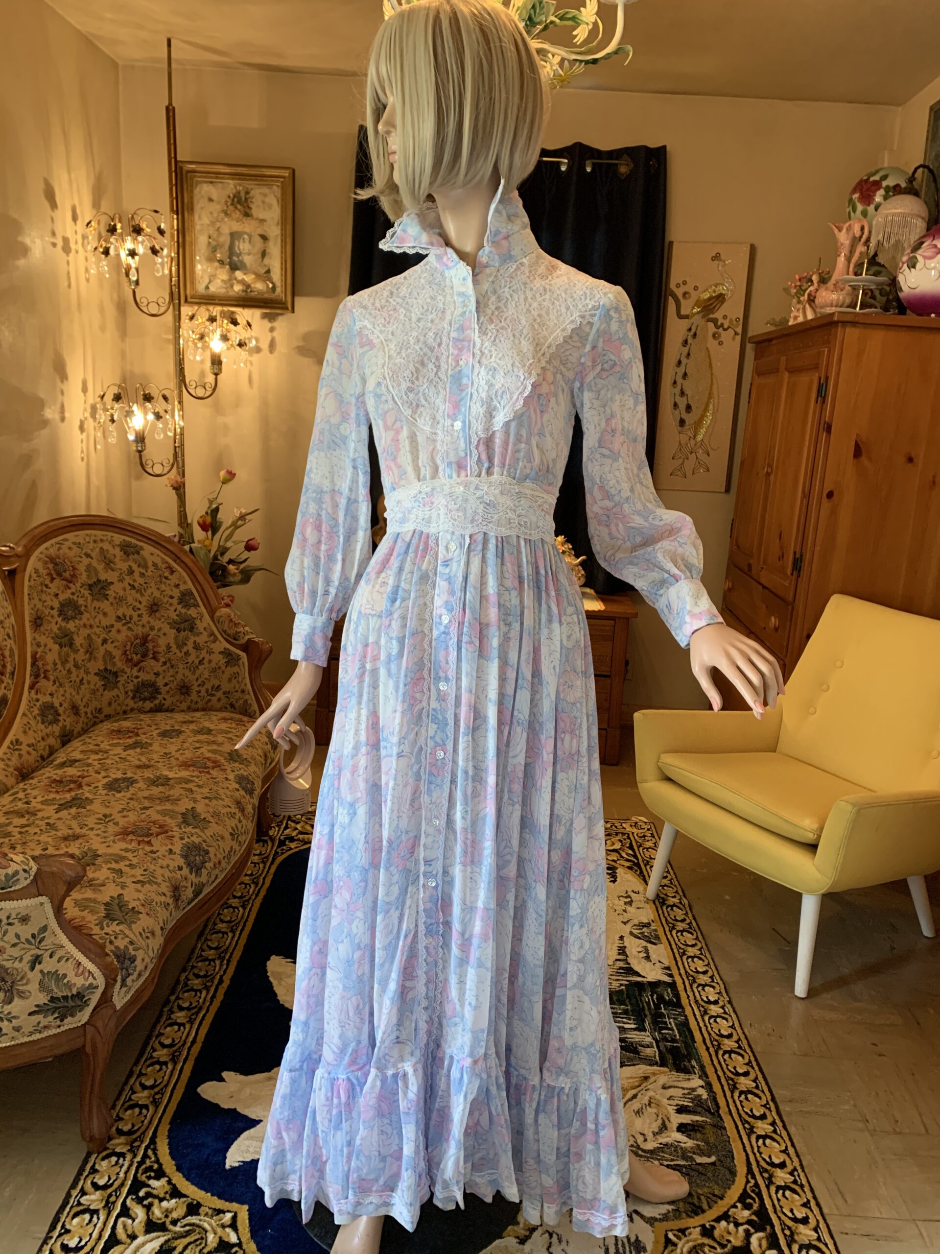 Handmade 1970s floral voile prairie dress with lace yoke, ruffled collar, long sleeves, and front button closure displayed in a vintage salon setting.