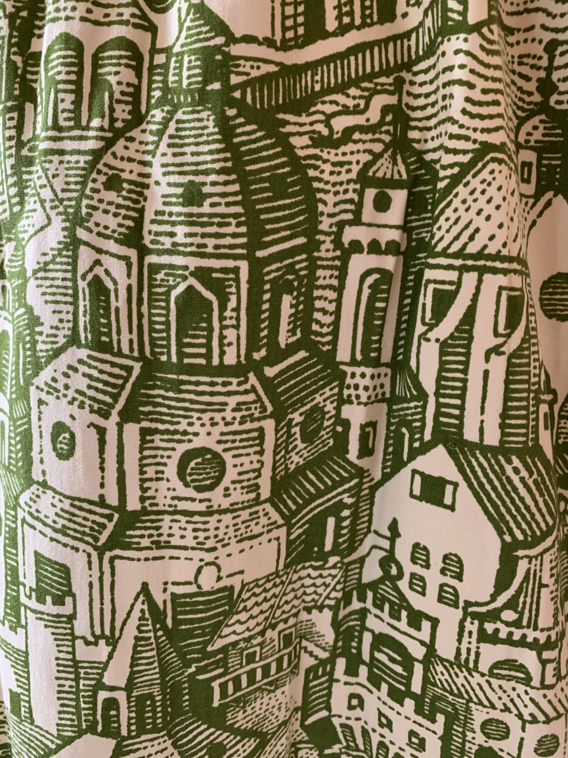 Side profile of 1970s handmade cotton maxi dress showcasing the flowing silhouette and detailed cityscape fabric design.
