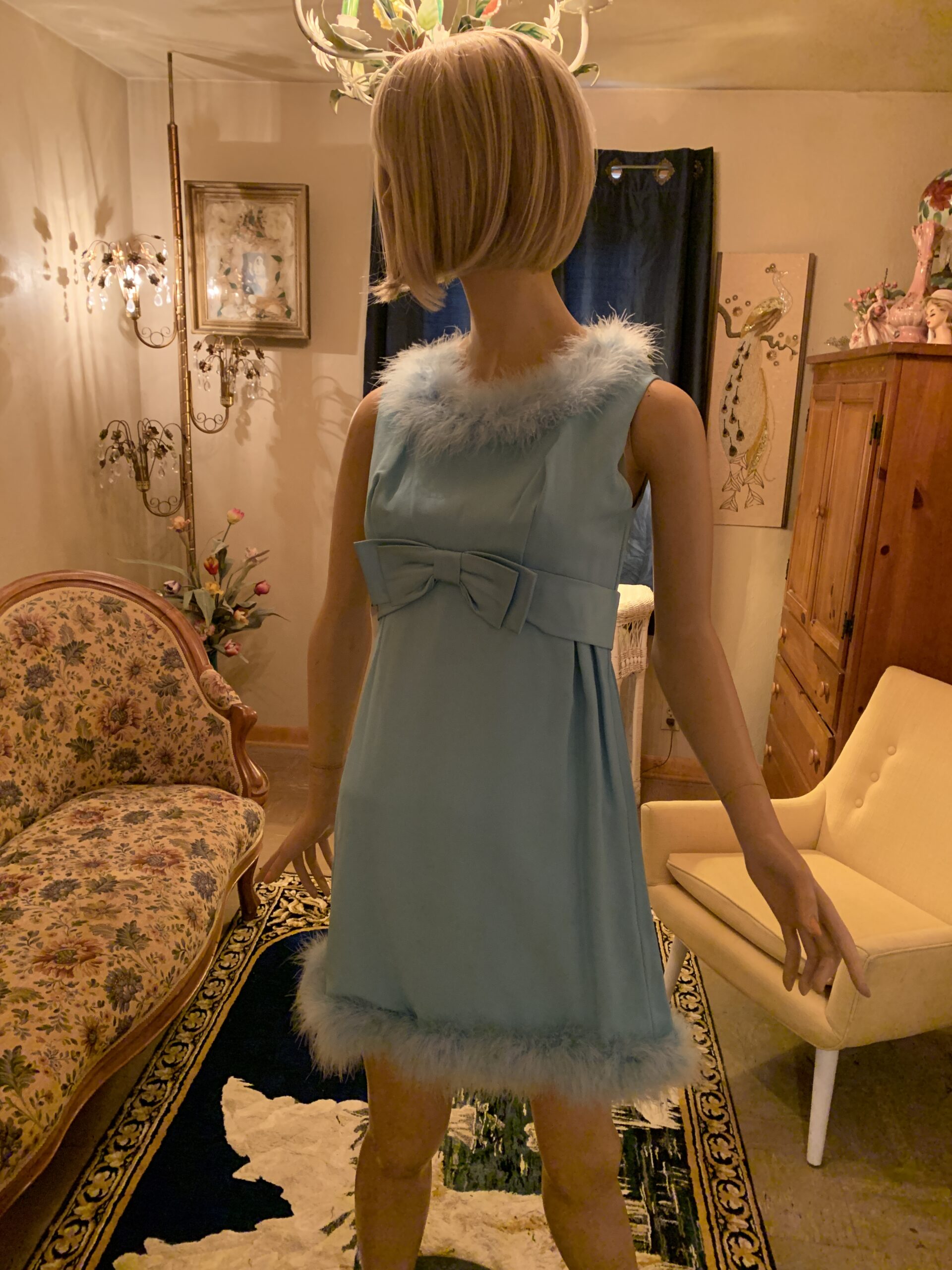 Vintage 1960s robin’s egg blue cocktail dress with marabou feather trim, empire waist bow, and sleeveless shift silhouette displayed on a mannequin.