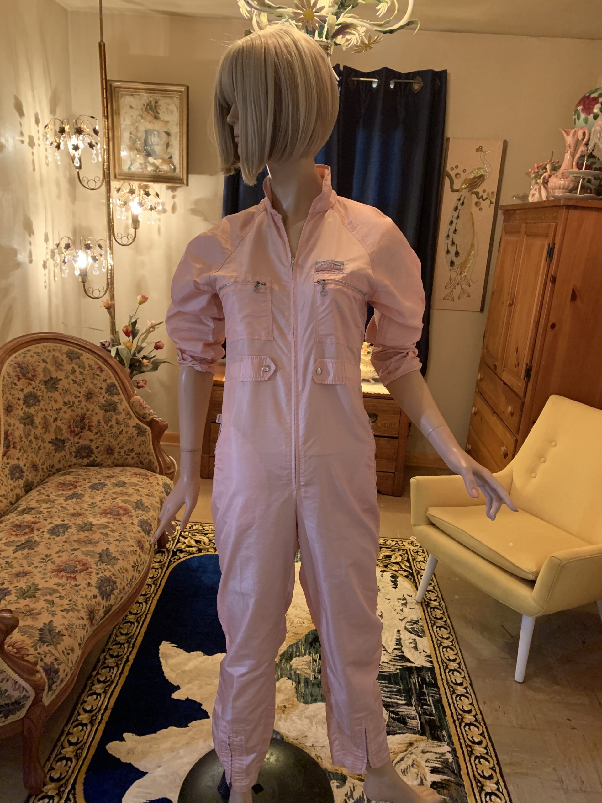 Front view of a vintage blush pink 1980s utility jumpsuit featuring zippered chest pockets, snap accents, stand collar, and front zip closure.