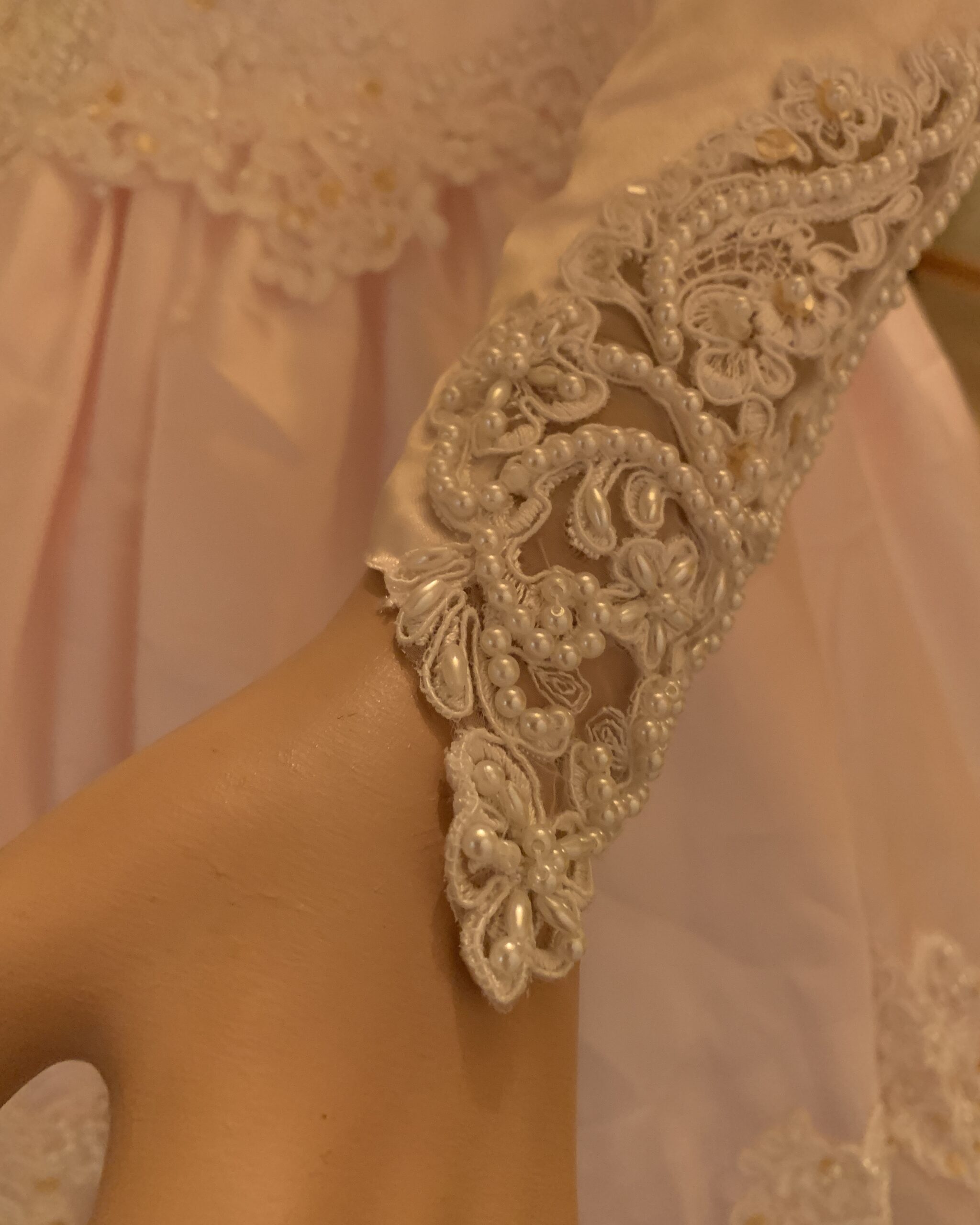 Close-up of lace cuff on vintage blush pink wedding gown featuring pearl beading, appliqué work, and sheer illusion detail.