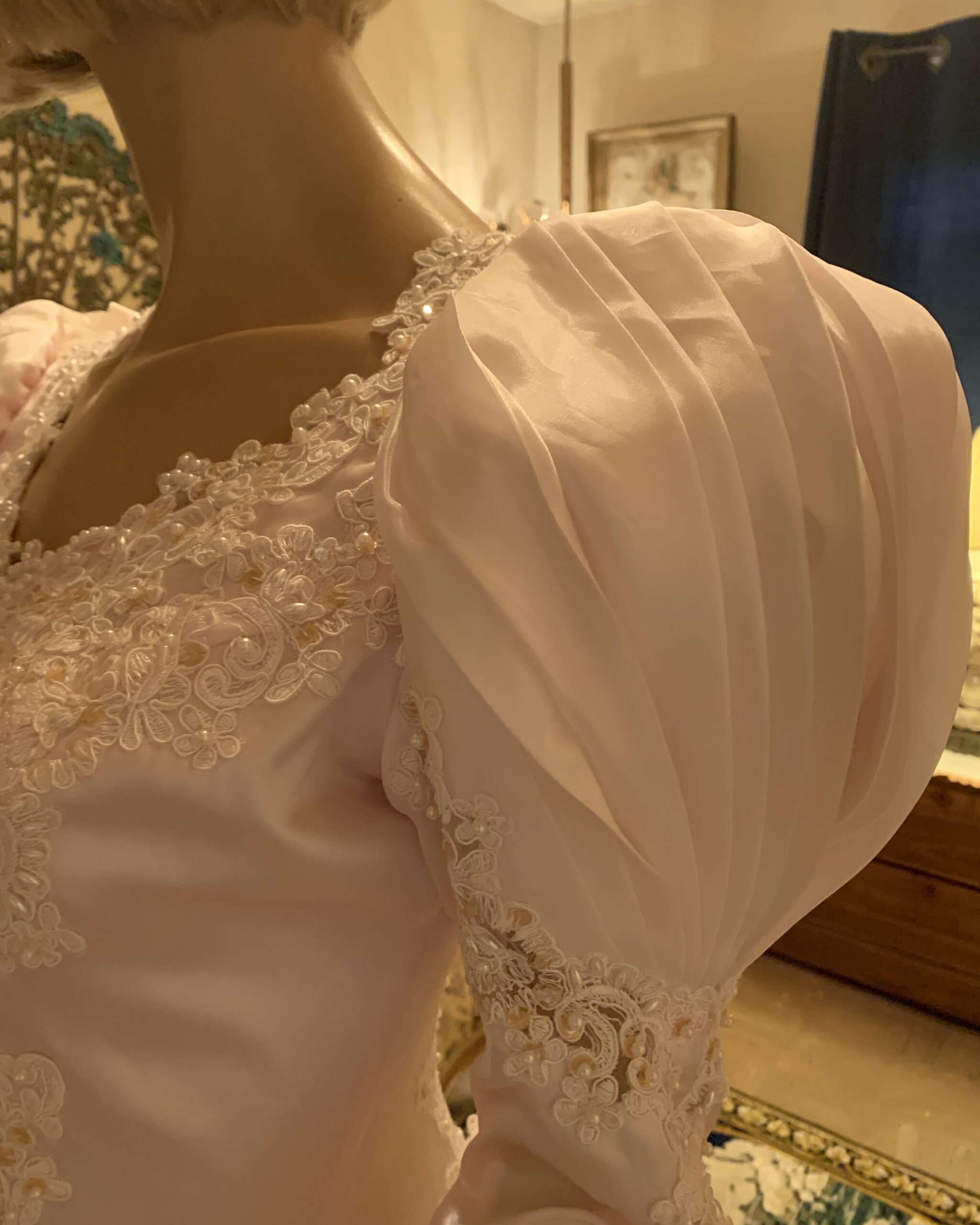 Close-up of sculptural puff sleeve on deadstock blush pink bridal gown with lace appliqué and pearl embellishment.