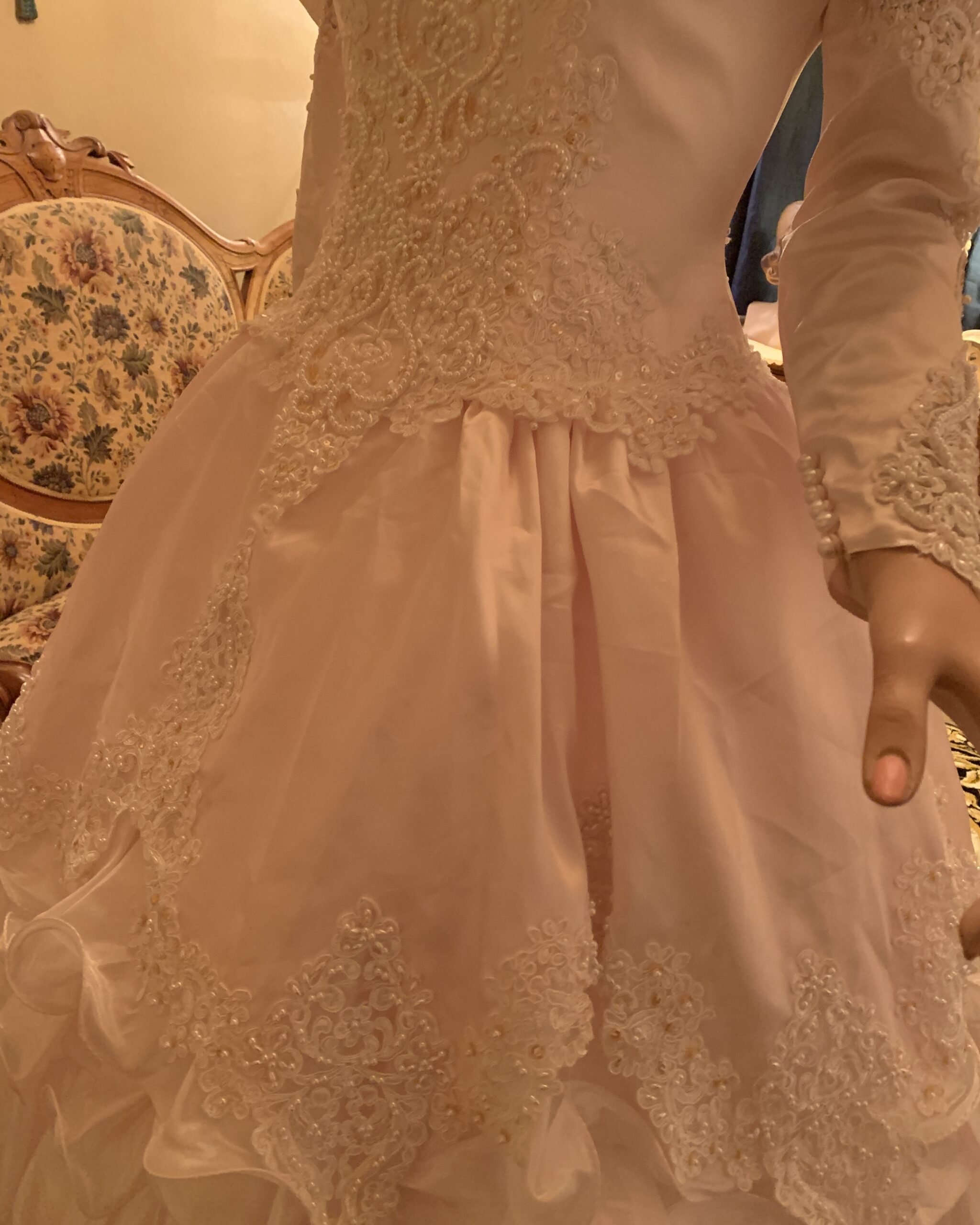 Detail of blush pink bridal gown skirt featuring lace appliqué panels, pearl embellishment, and cascading organza ruffles.