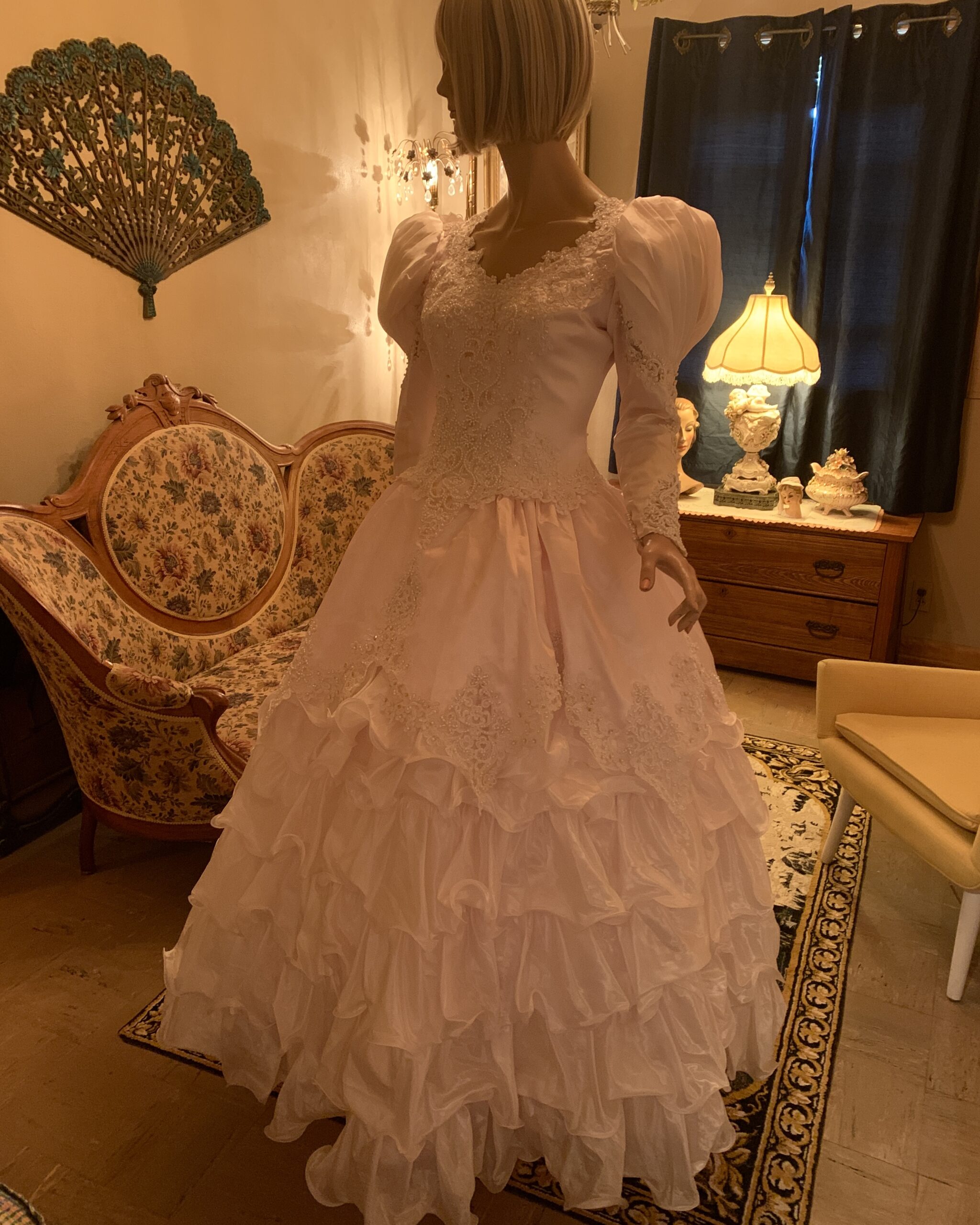 Vintage blush pink deadstock bridal gown with beaded lace bodice, puff sleeves, and dramatic tiered ruffle skirt displayed on mannequin.