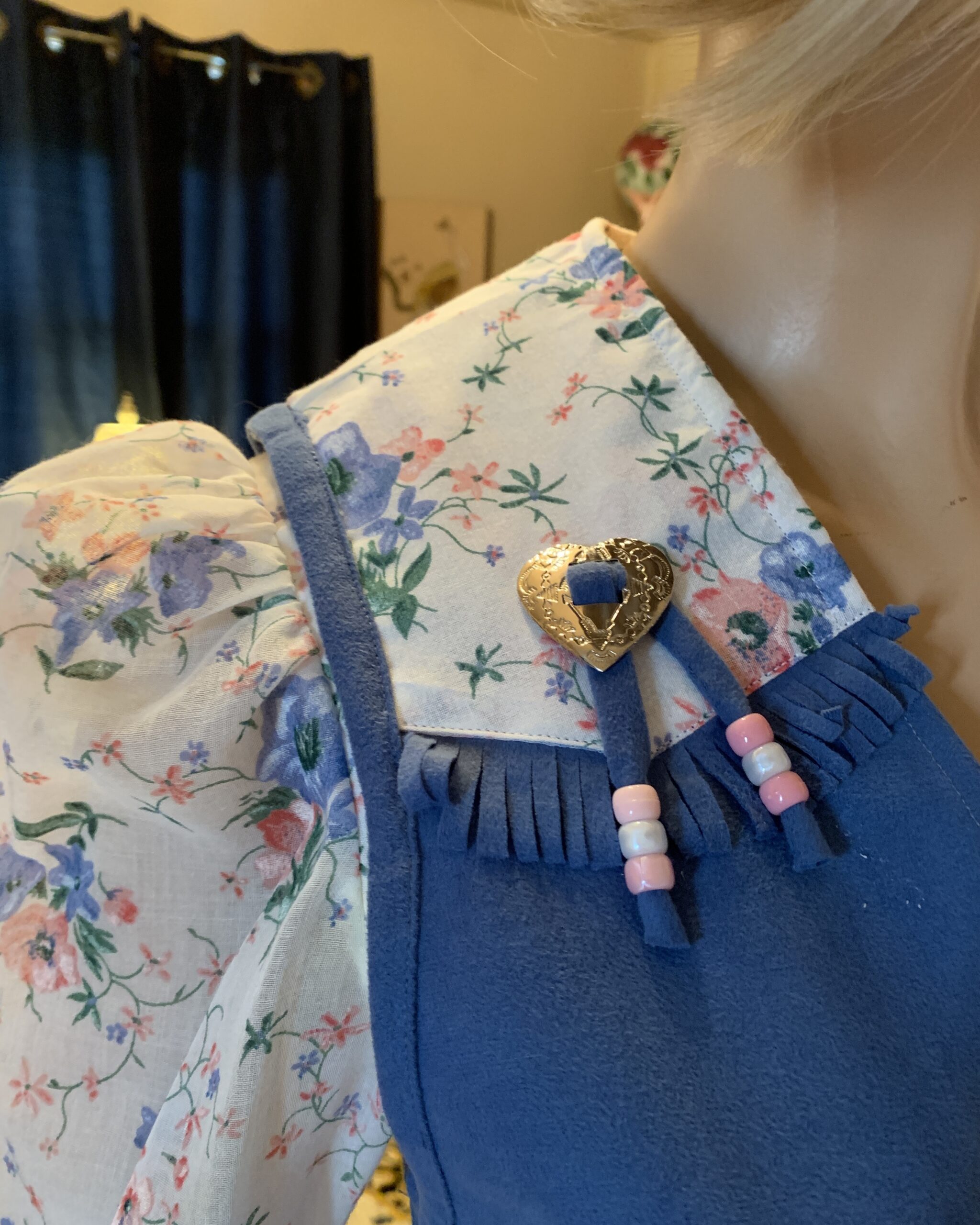 Close-up of removable western-style vest with heart-shaped concho, fringe trim, and pink and pearl bead accents.