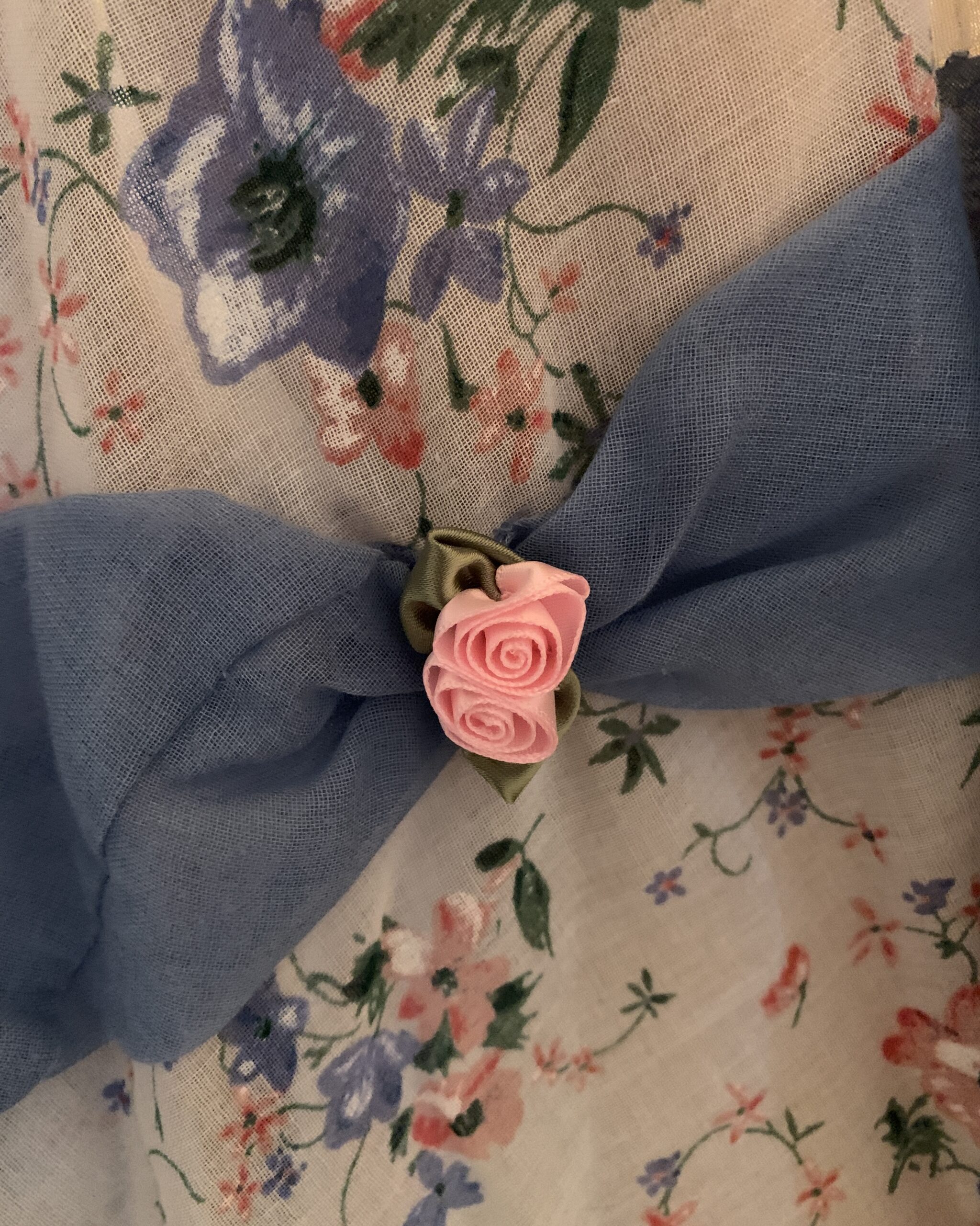 Close-up of pink ribbon rose embellishment attached to blue voile trim on handmade floral prairie dress.