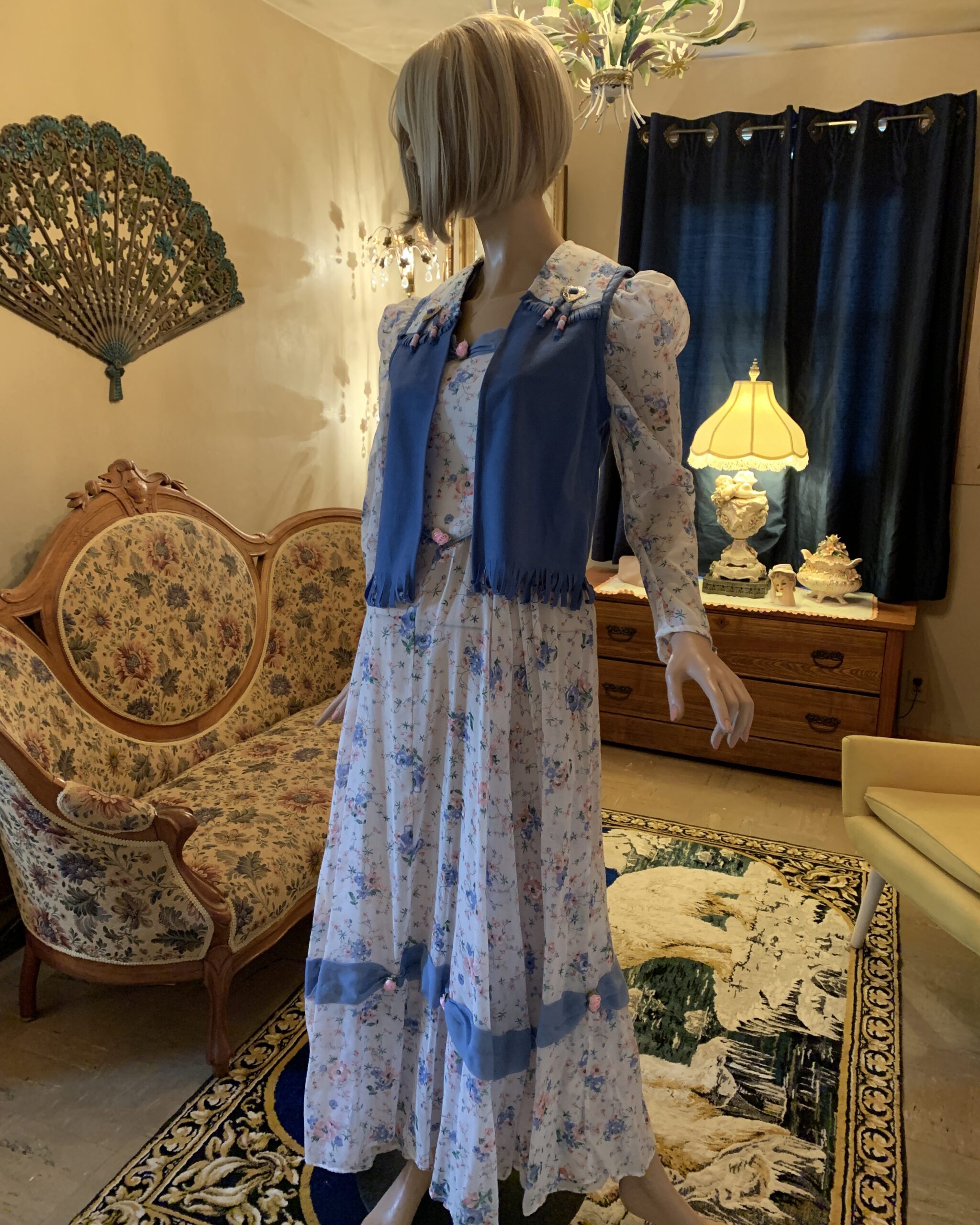 Western-inspired floral prairie dress with removable blue vest, showcasing layered styling and handmade decorative details.