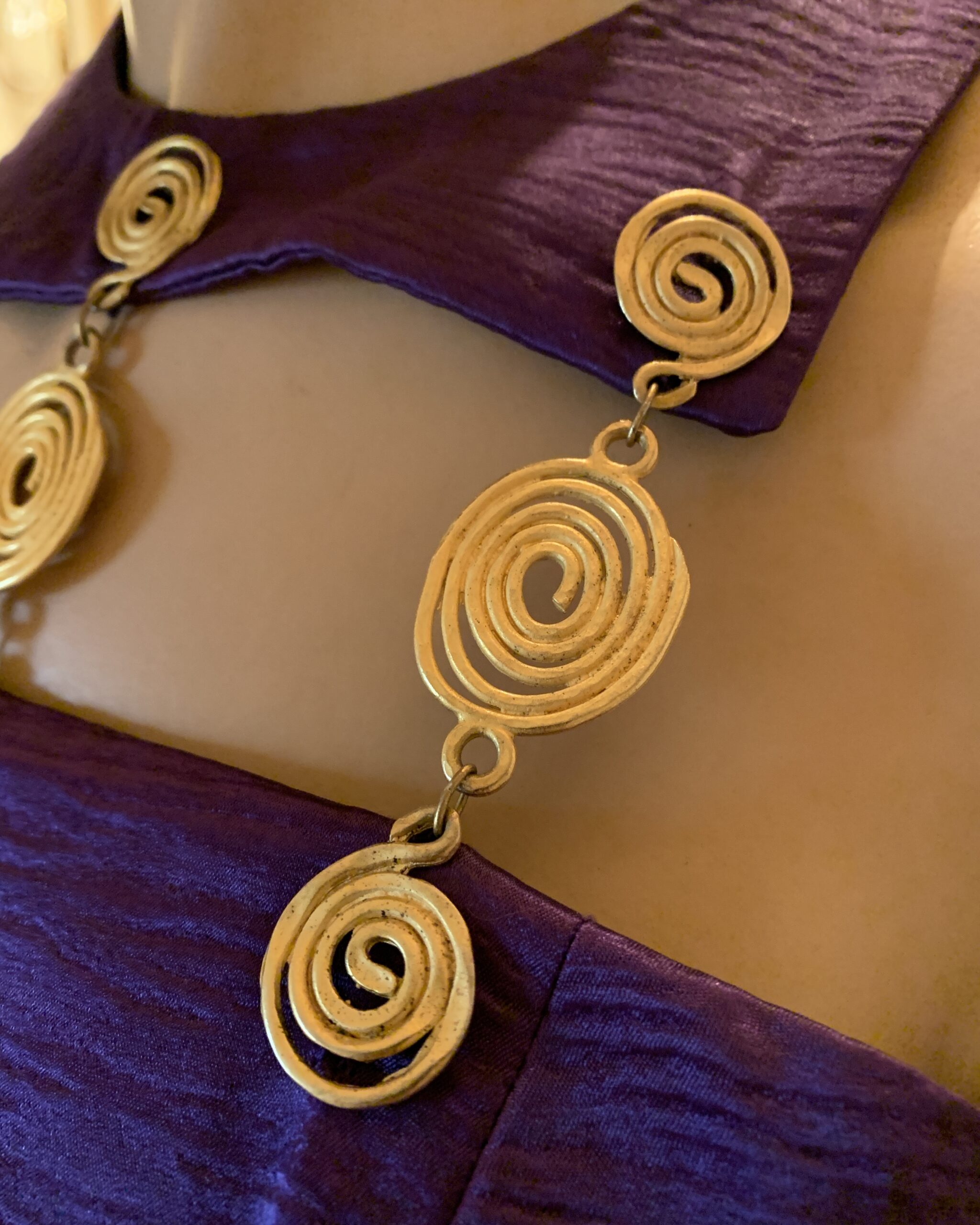 Close-up of the sculptural gold spiral neckline on a 1980s Linda Separates violet sheath dress, highlighting the architectural cutout design and textured violet fabric.