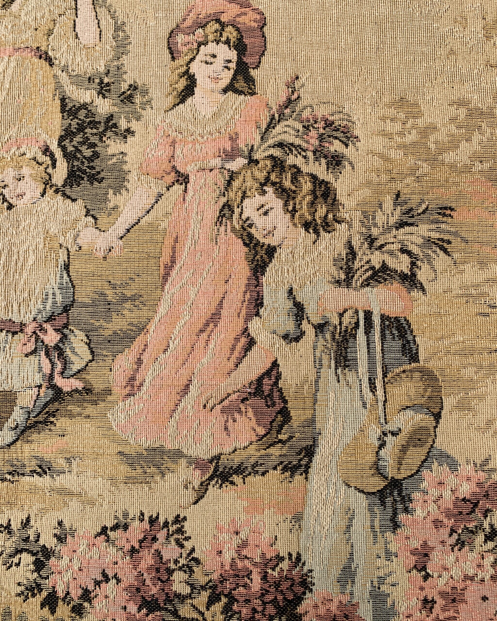 Close-up of a vintage woven wall hanging showing women and children gathering flowers in a romantic pastoral garden scene.