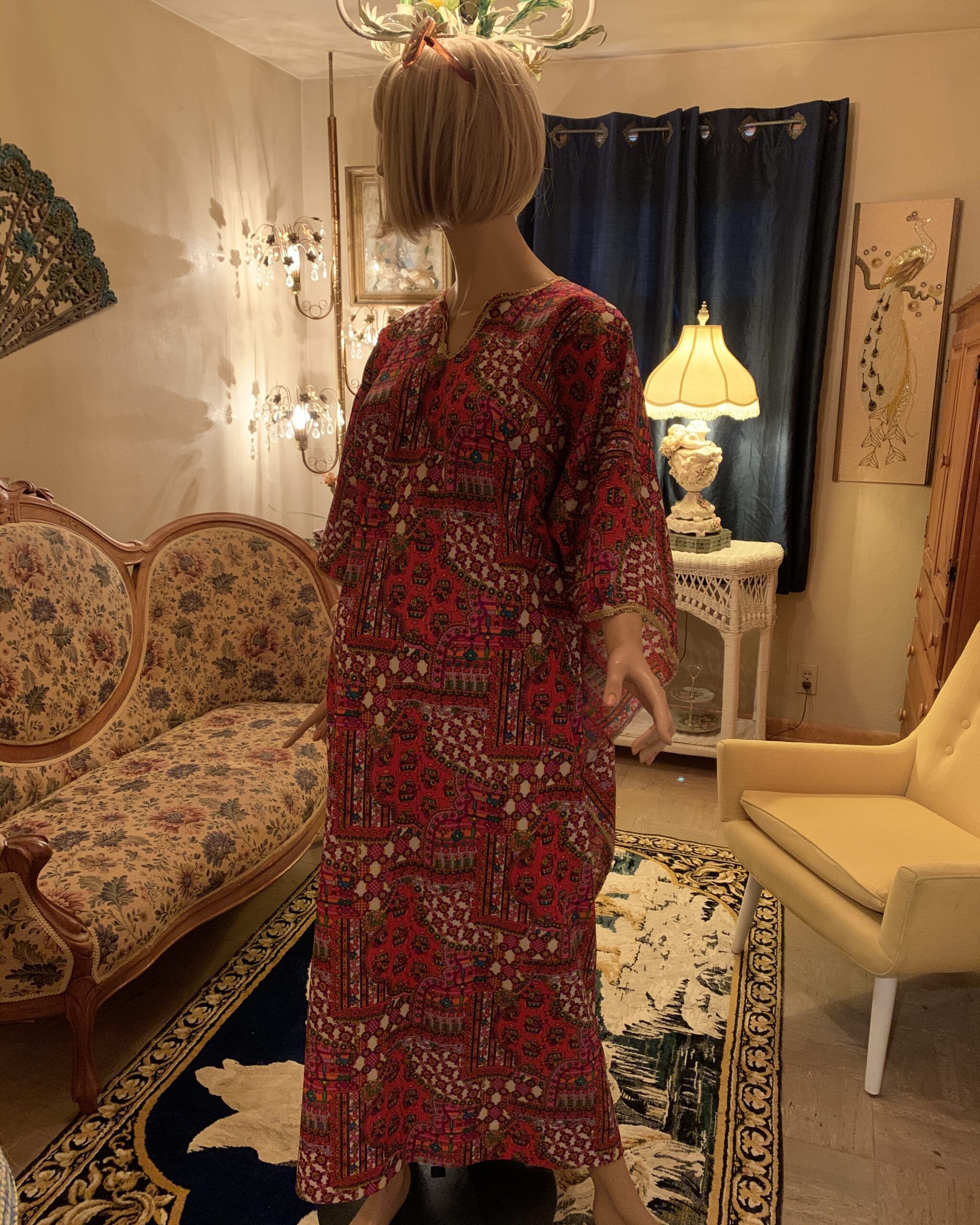 Three-quarter view of a vintage 1970s polyester hostess caftan featuring a vibrant pink and red geometric print with wide sleeves and gold trim.