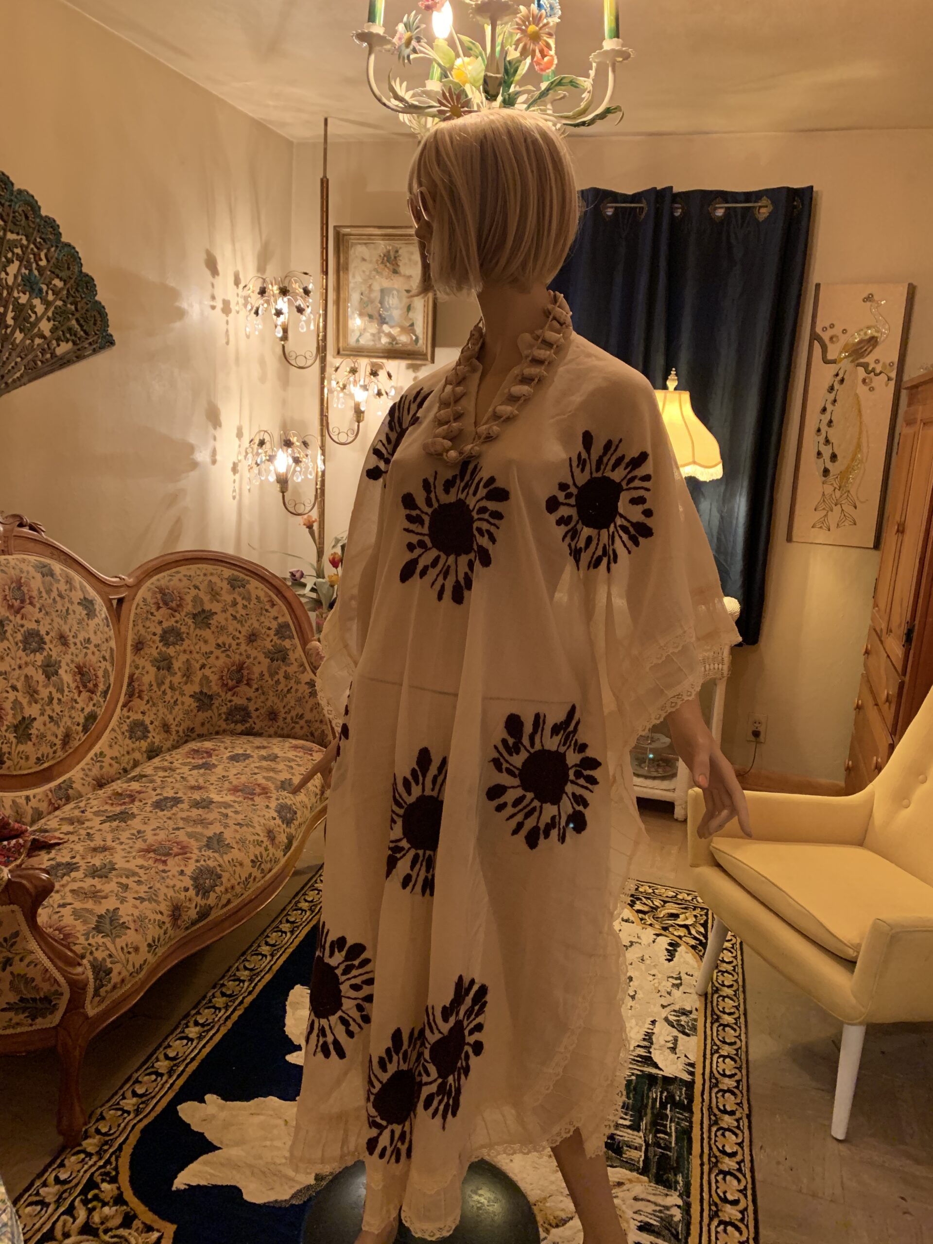 Vintage ivory cotton caftan with black floral embroidery, flowing cape sleeves, and lace trim displayed on a mannequin.