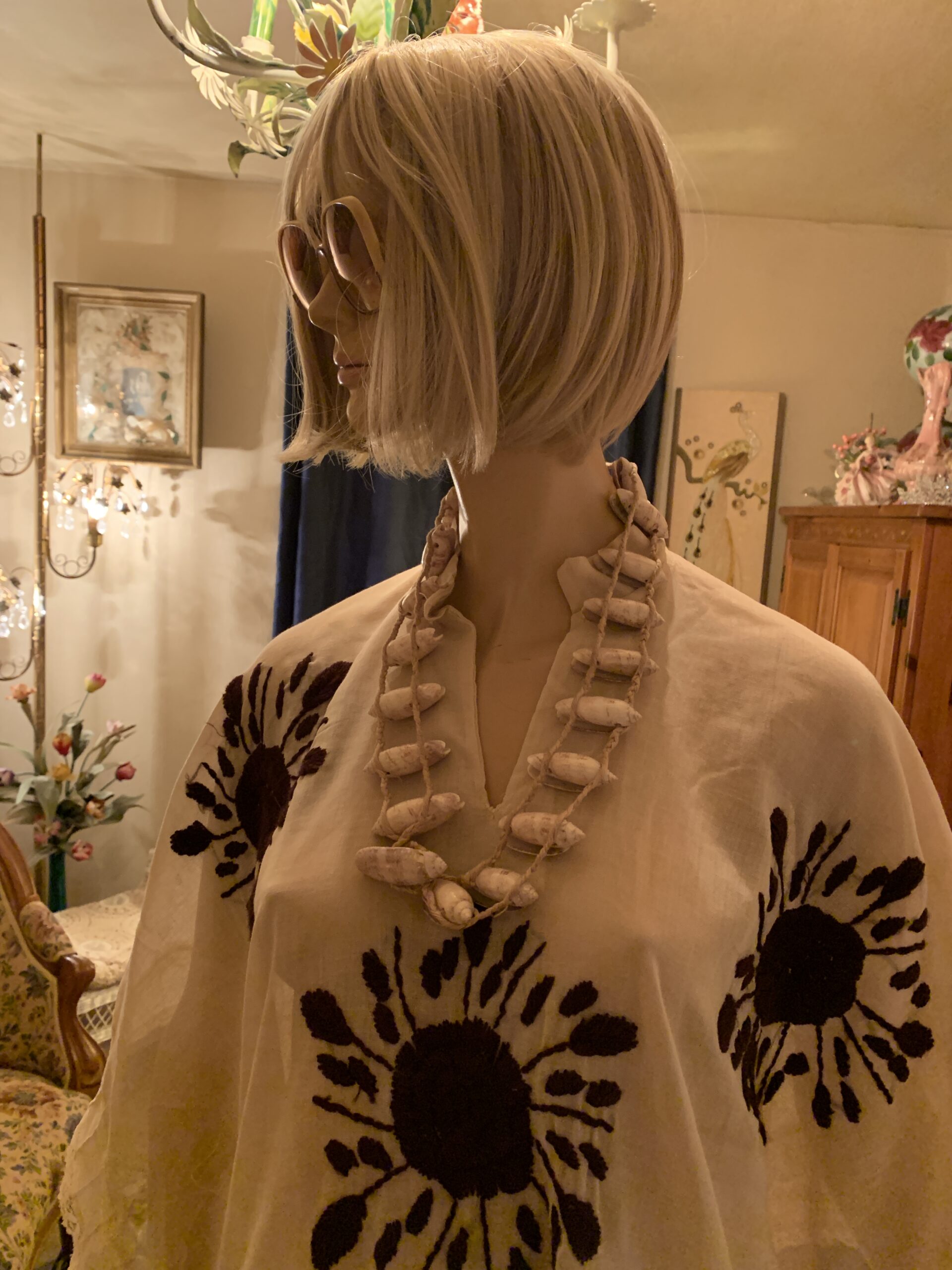 Close-up of the vintage ivory cotton caftan featuring a split neckline, black floral embroidery, and handcrafted shell necklace.