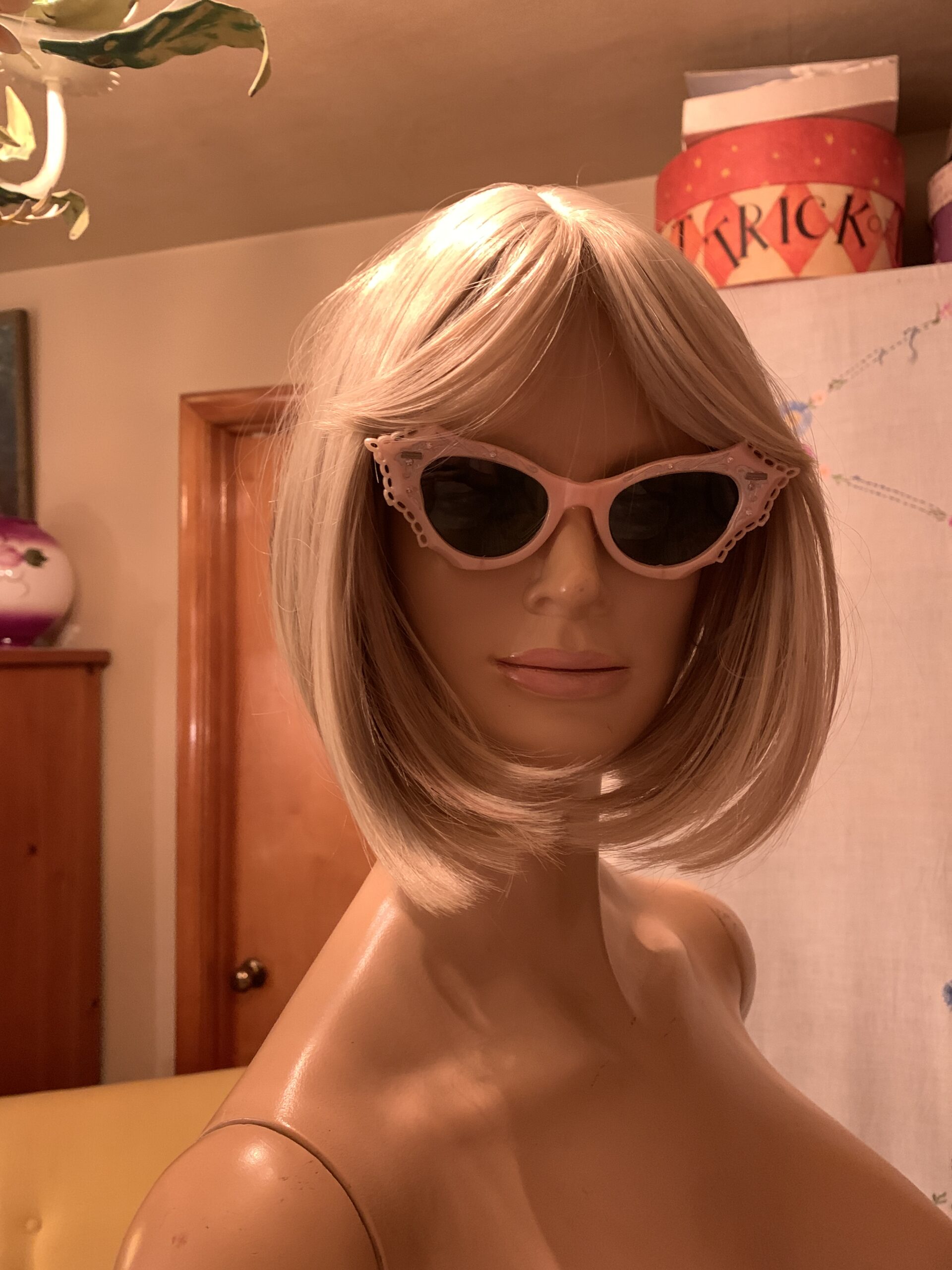 Side angle of vintage 1950s pink cat-eye sunglasses with pierced detailing and green lenses on a mannequin
