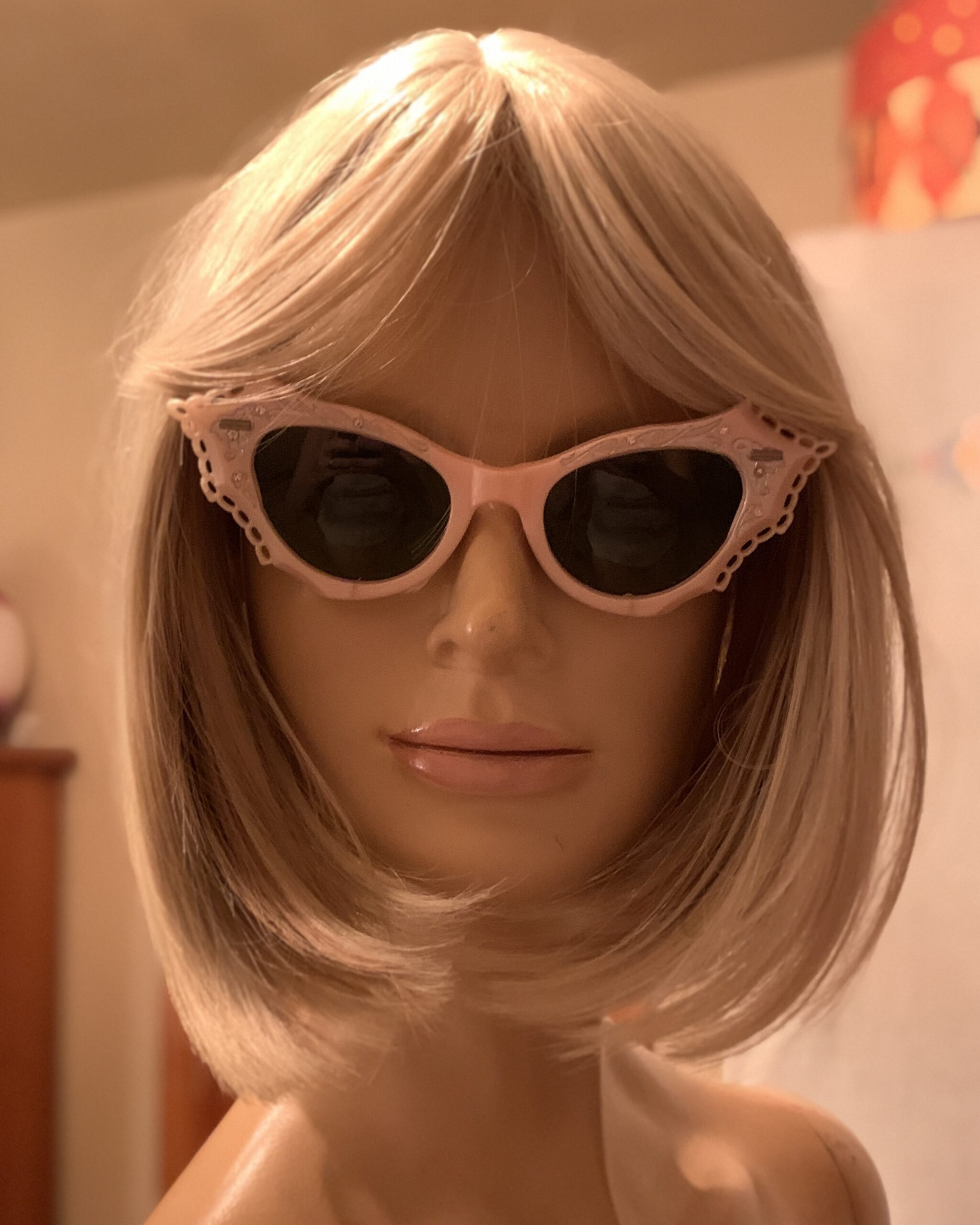 Vintage 1950s pink cat-eye sunglasses with dark green lenses displayed on a blonde mannequin.
