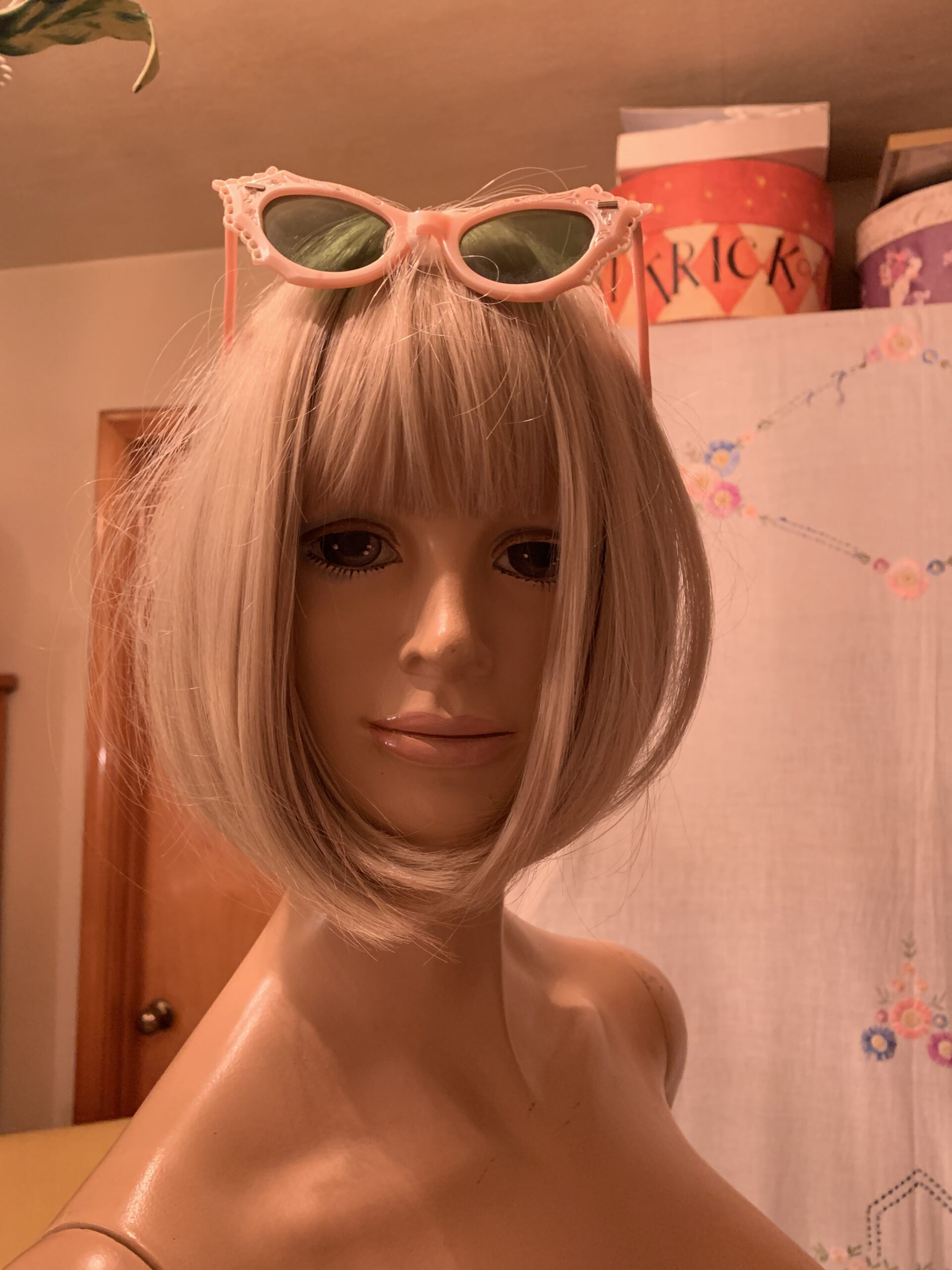 Vintage 1950s pink cat-eye sunglasses shown resting on top of a blonde mannequin’s head.