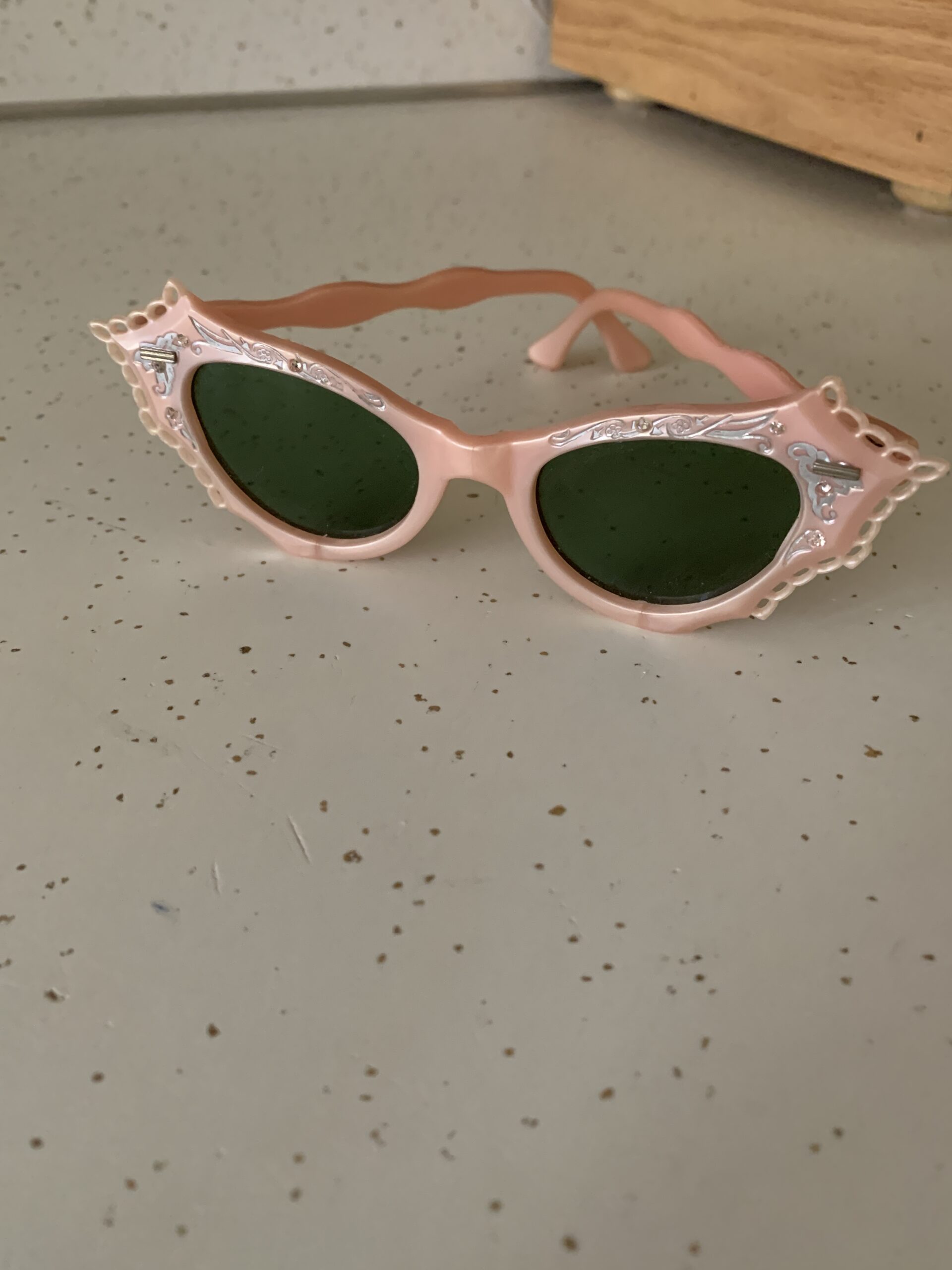 Vintage 1950s pink cat-eye sunglasses with decorative pierced corners and dark green lenses.