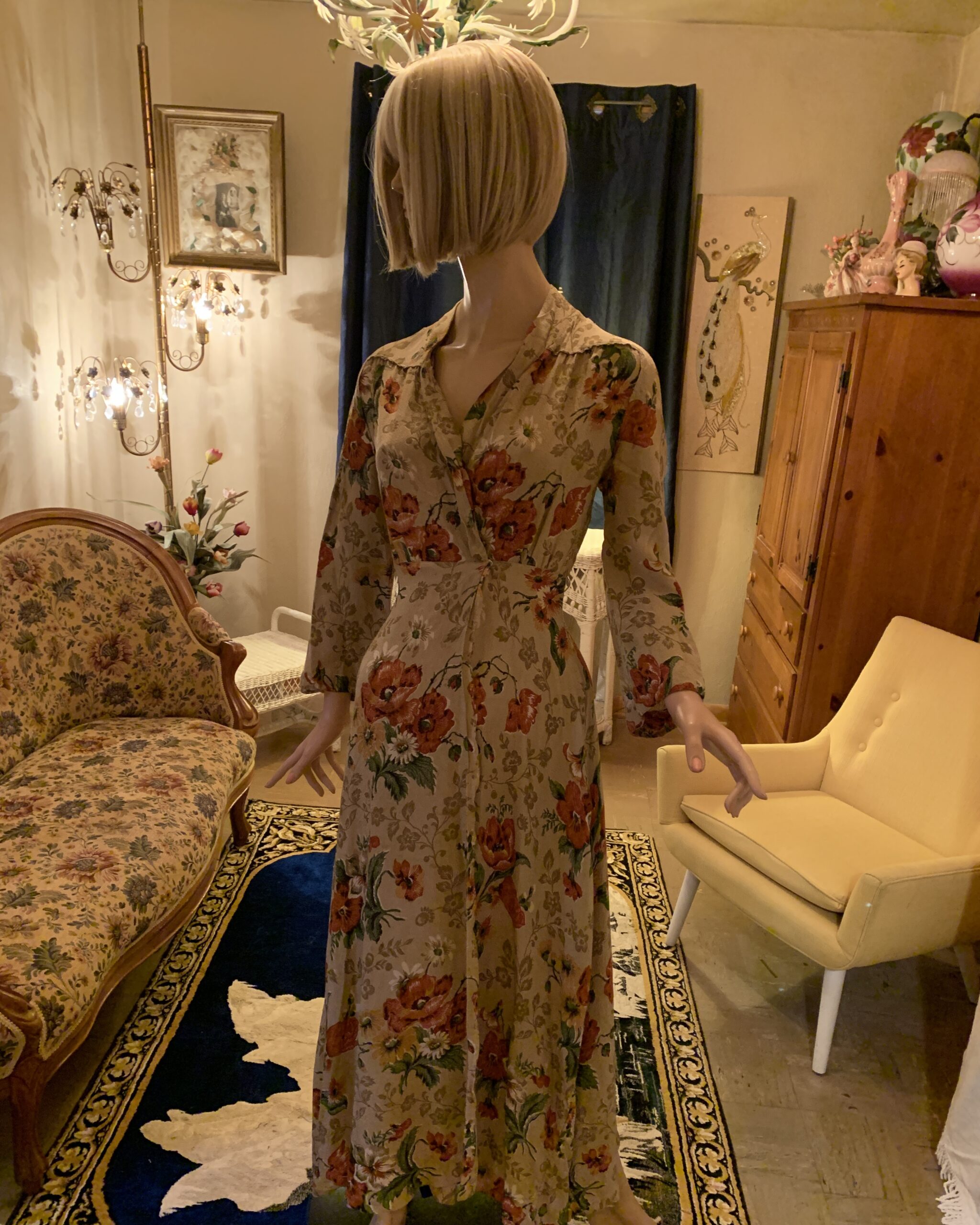 1940s floral wrap dress with a beige background, rust-red poppy print, long sleeves, and a flowing midi-length skirt displayed on a mannequin in an editorial vintage salon.