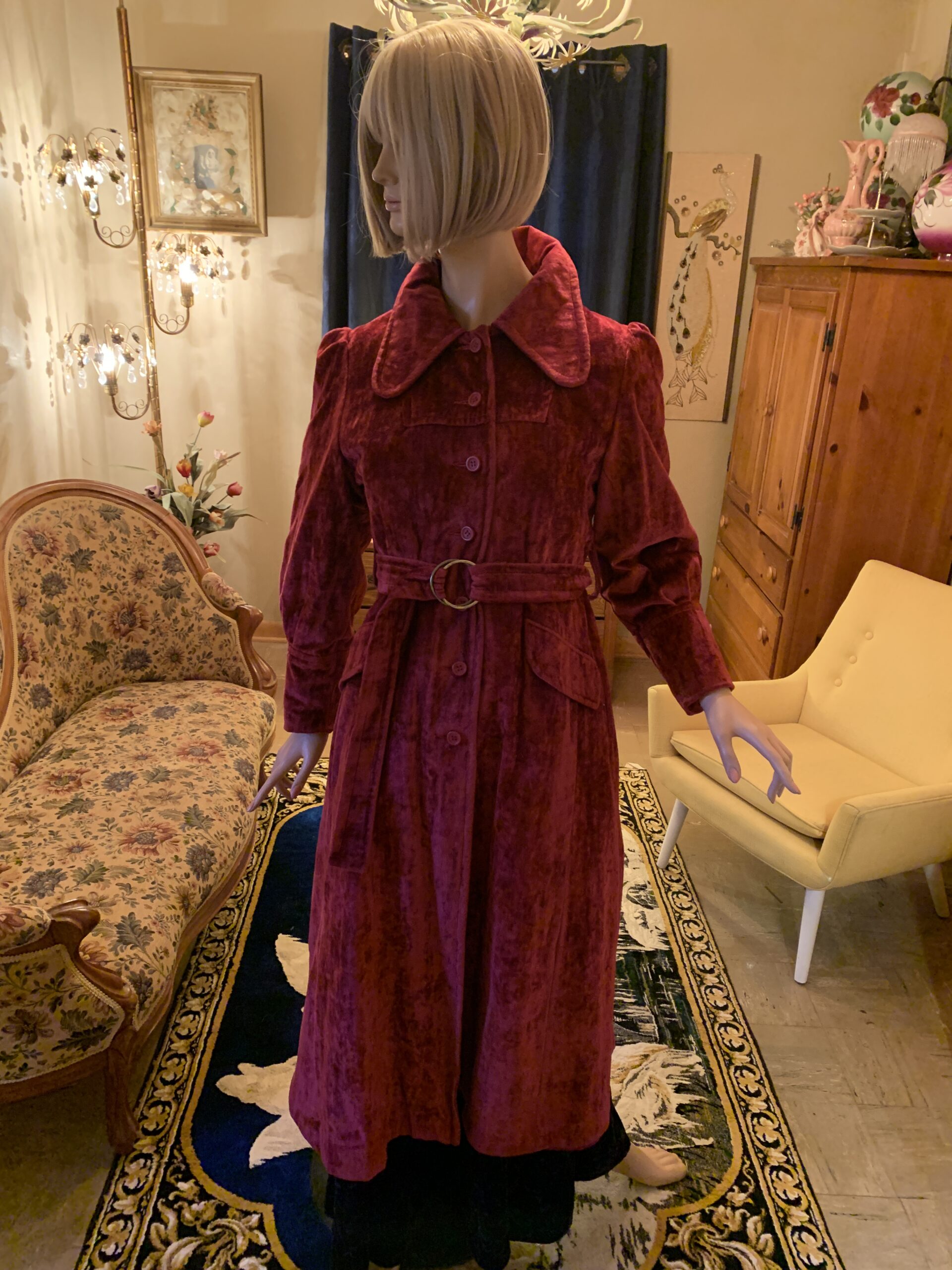 1970s burgundy crushed velvet belted coat with oversized rounded collar, puff sleeves, and button front displayed on a mannequin.