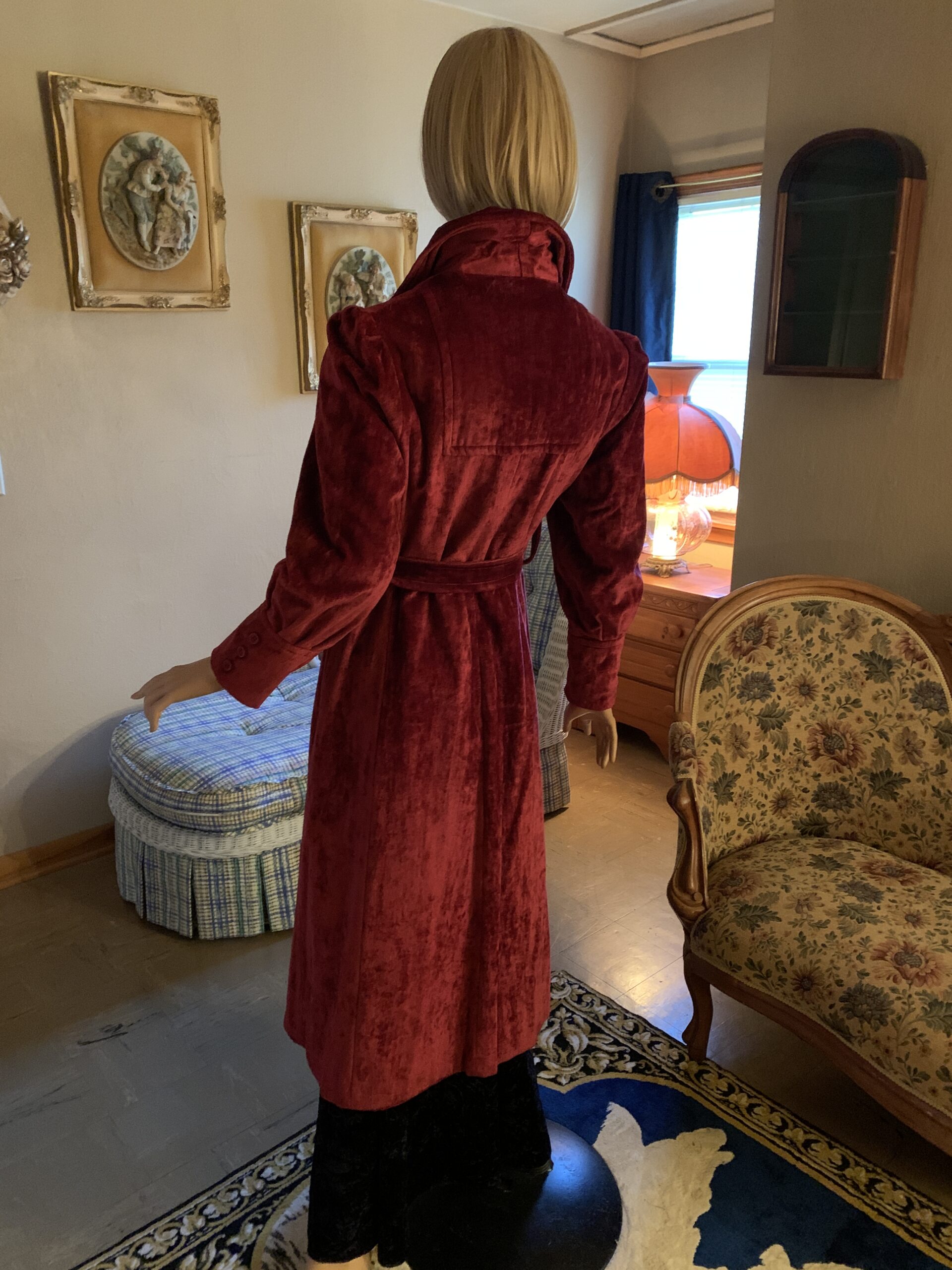 Back view of a 1970s burgundy crushed velvet coat showing the fitted waist, full-length silhouette, and gathered shoulders.