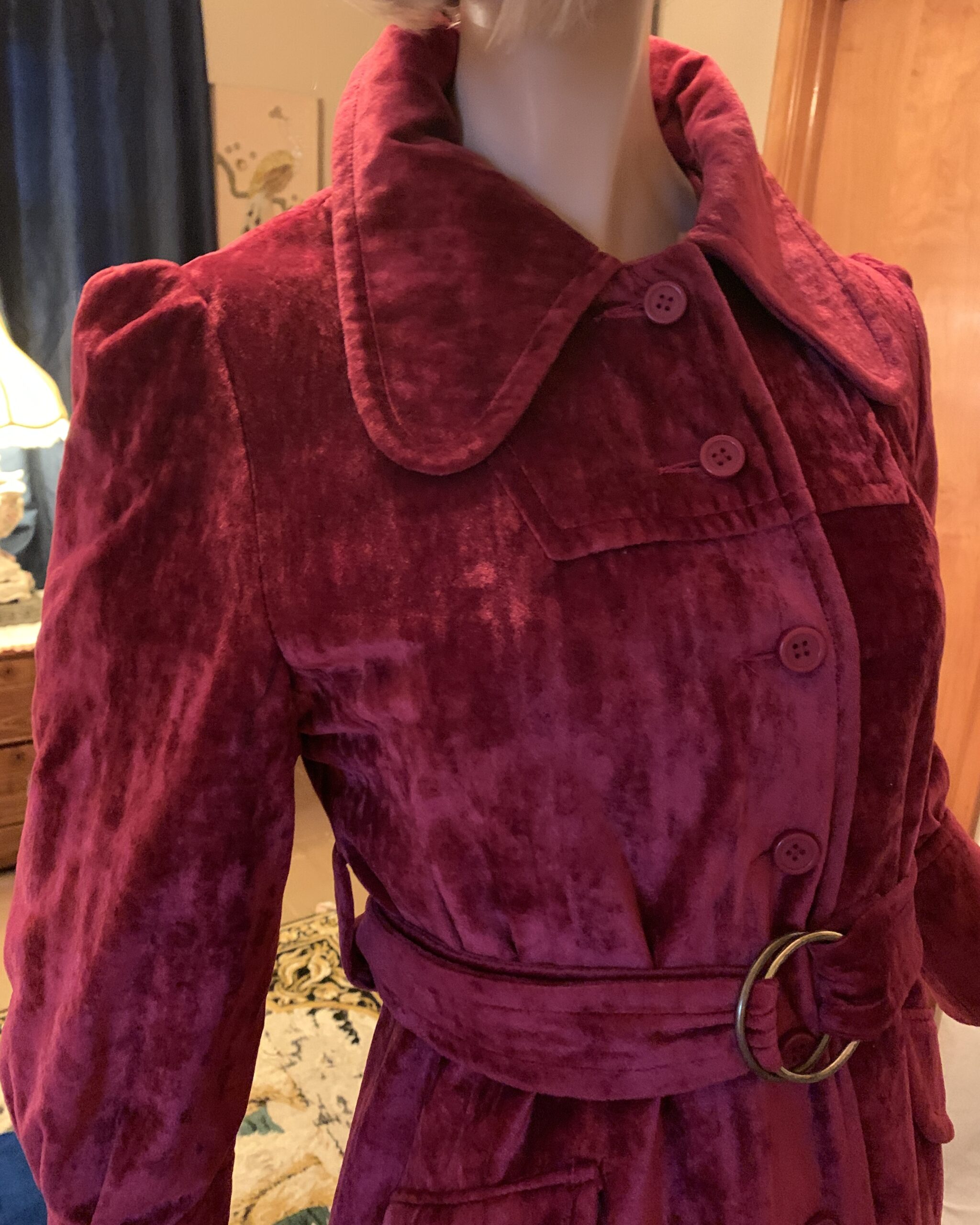 Close-up of the oversized rounded collar, covered buttons, and self belt with circular buckle on a 1970s burgundy crushed velvet coat.