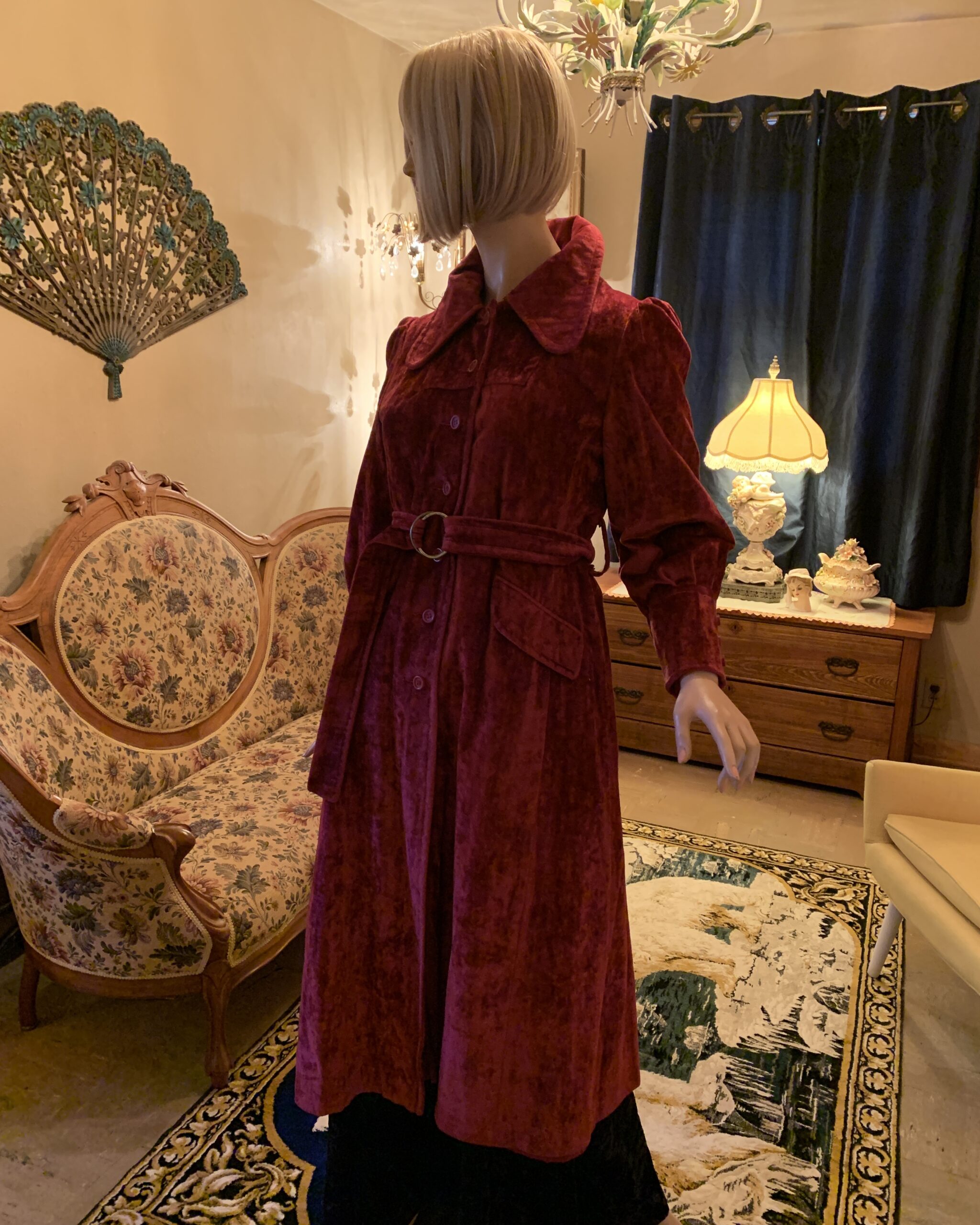 Three-quarter view of a 1970s burgundy crushed velvet coat featuring a belted waist, dramatic rounded collar, and tailored silhouette.