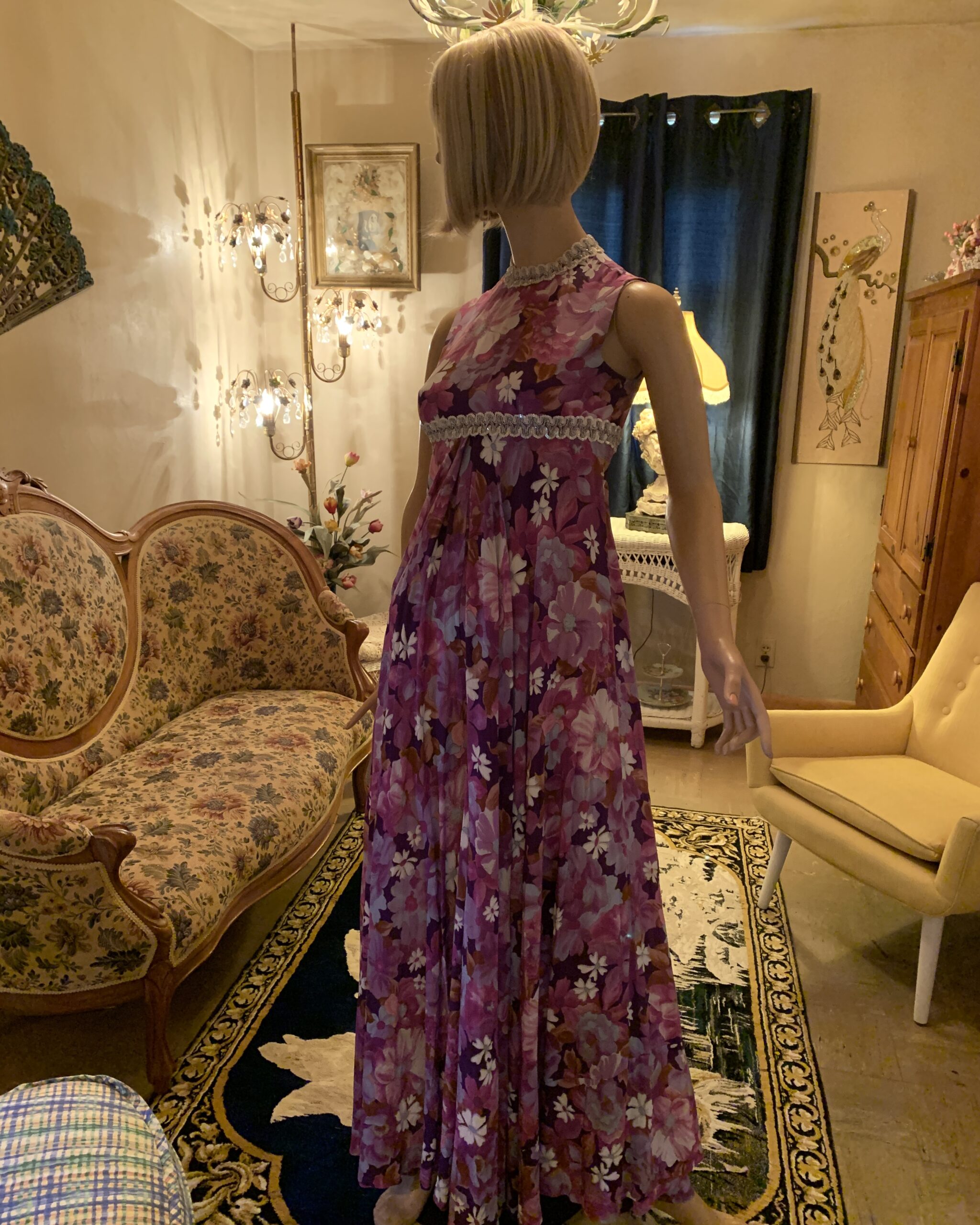 Full-length view of a 1970s purple floral jumpsuit with a high neckline, empire waist, and sweeping wide legs.