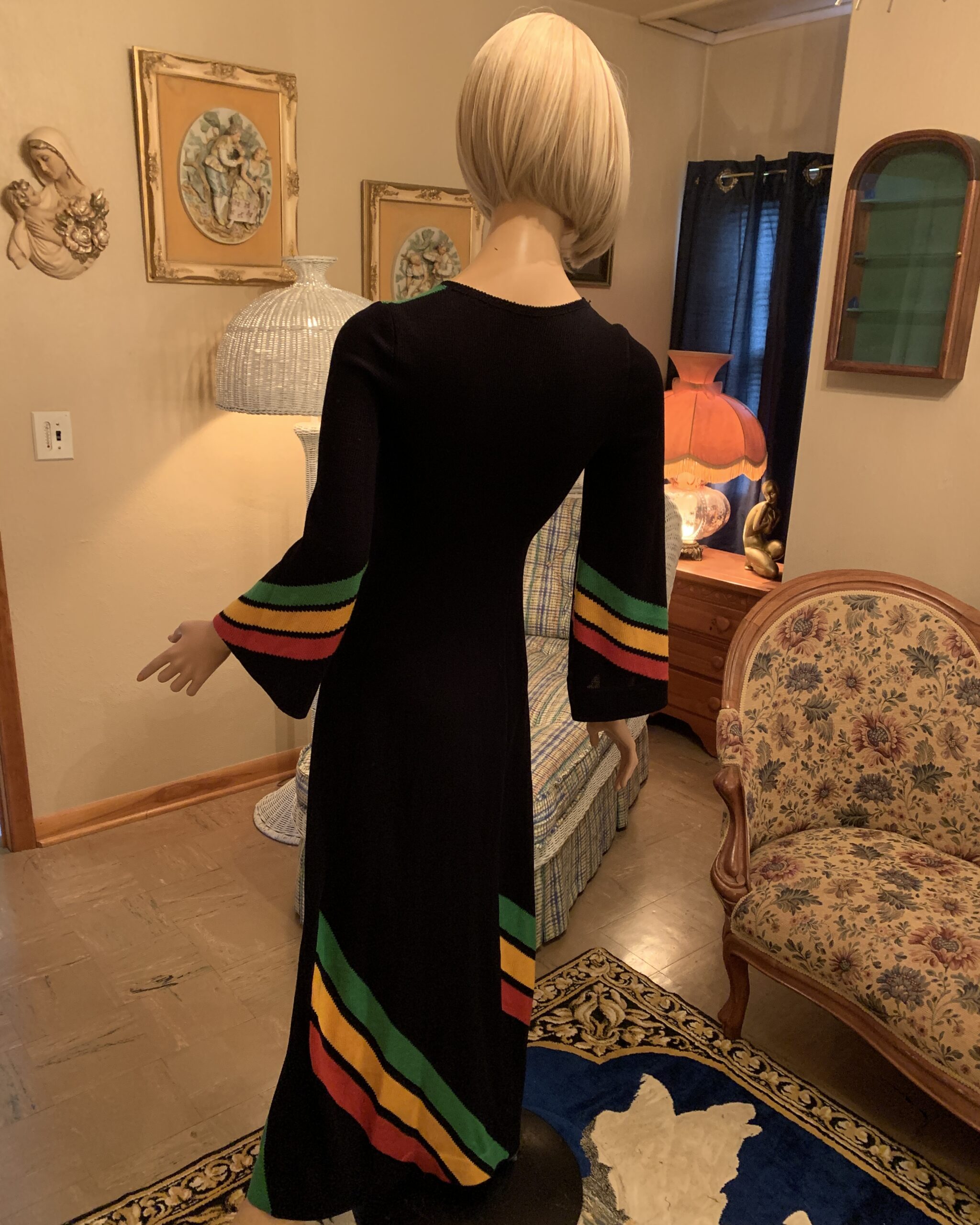 Back view of late 1960s to early 1970s black knit maxi dress showing long silhouette, flared sleeves and colorblock hem design.