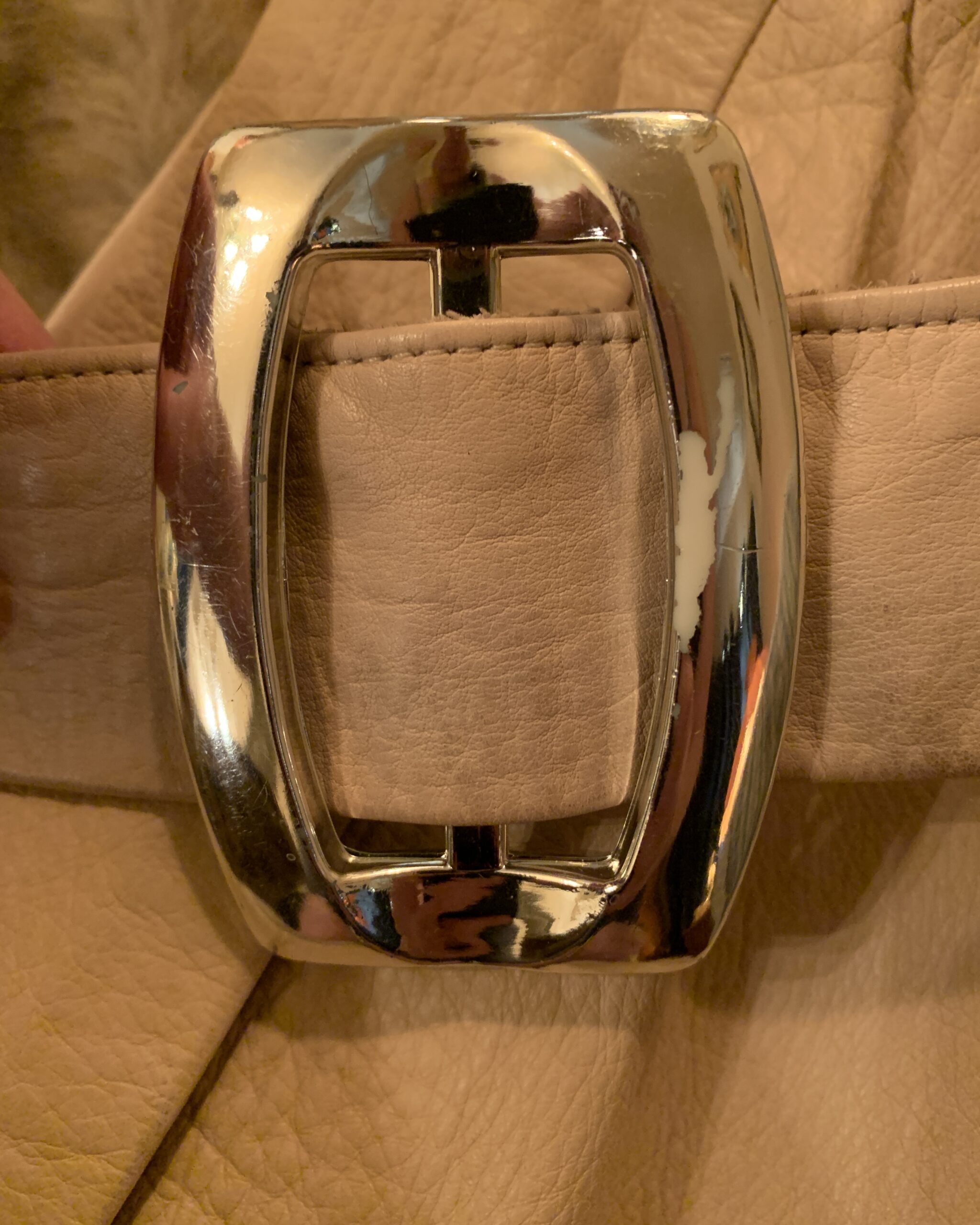 Close-up of the original chrome belt buckle showing light age-related finish wear on the vintage Lilli Ann London leather coat.