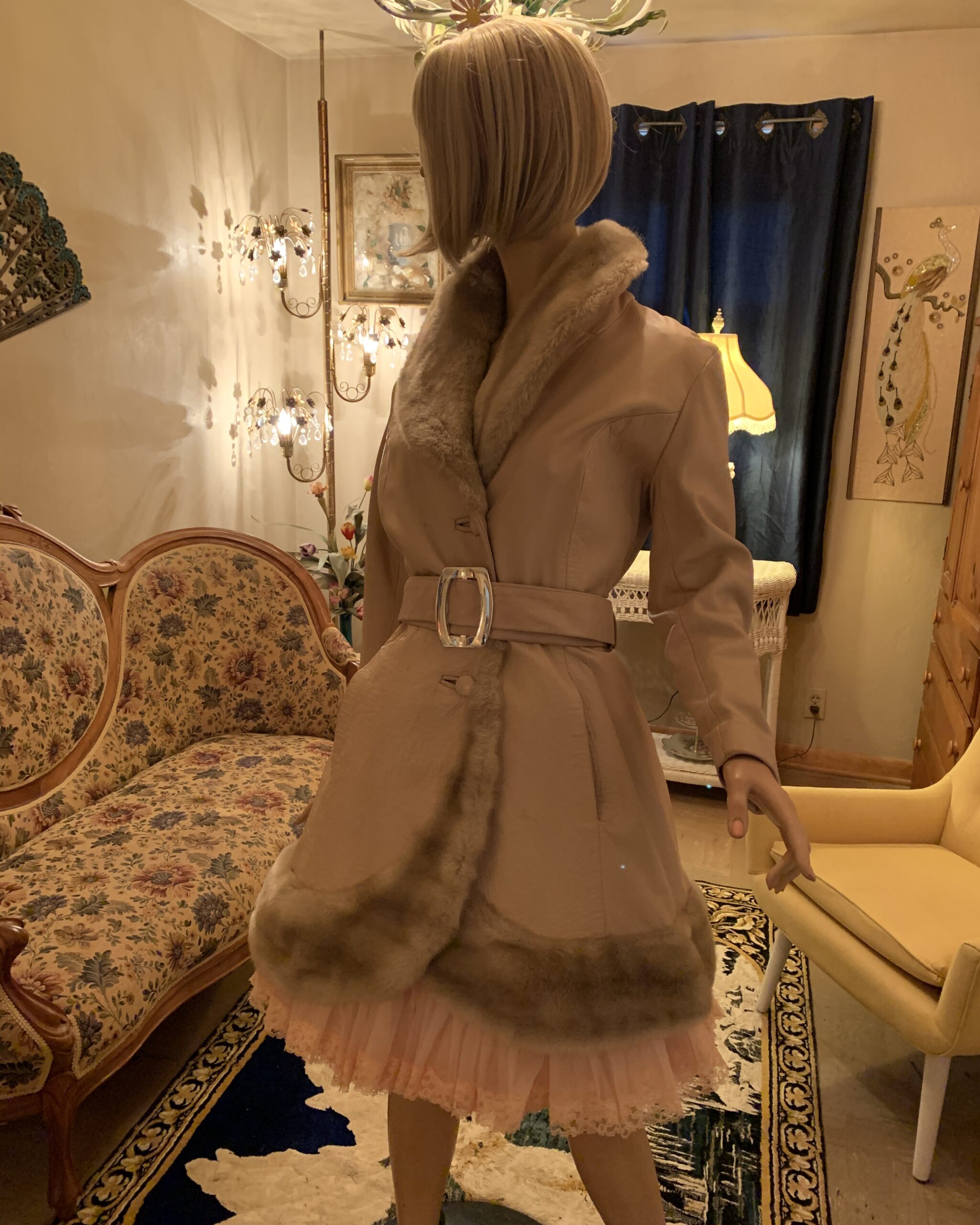 Three-quarter view of a vintage Lilli Ann London champagne leather coat with sculptural shawl collar, fur trim, and statement buckle.