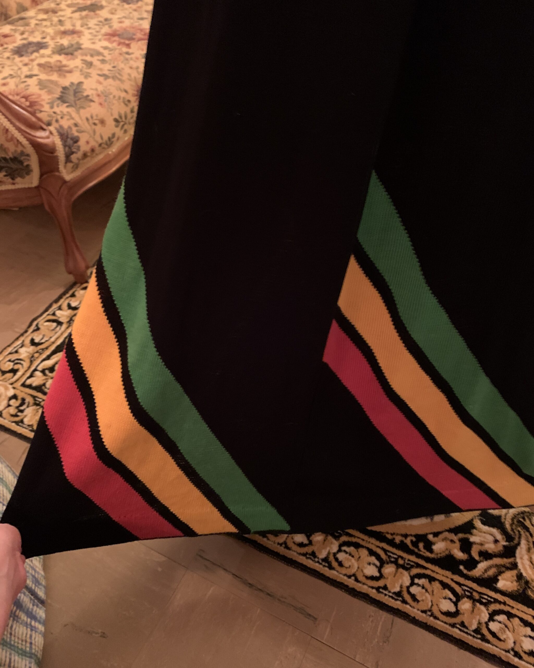 Close-up of sweeping green, golden yellow and red knitted colorblock design at the hem of vintage black maxi dress.