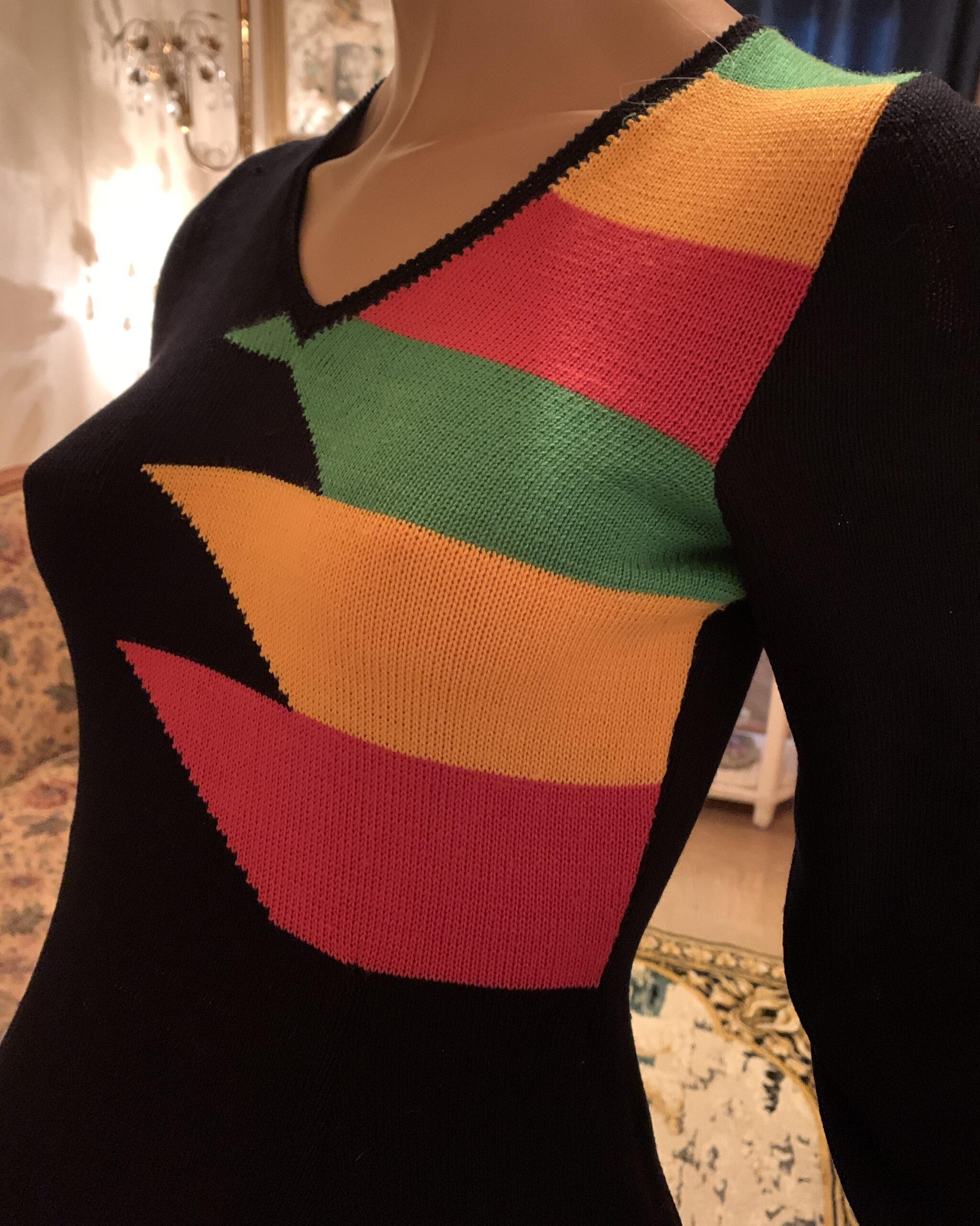 Close-up of vintage modernist knit maxi dress showing asymmetric green, red and golden yellow geometric colorwork across the bodice.