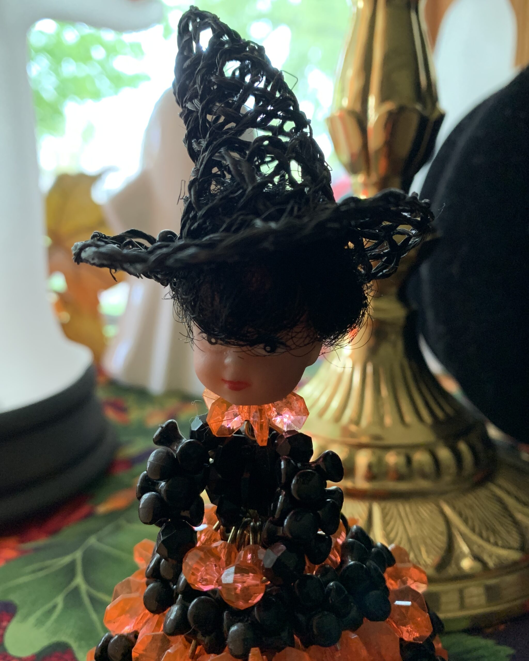 Close view of the witch doll’s painted face, black beaded bodice, orange crystal-style bead collar, and woven witch hat