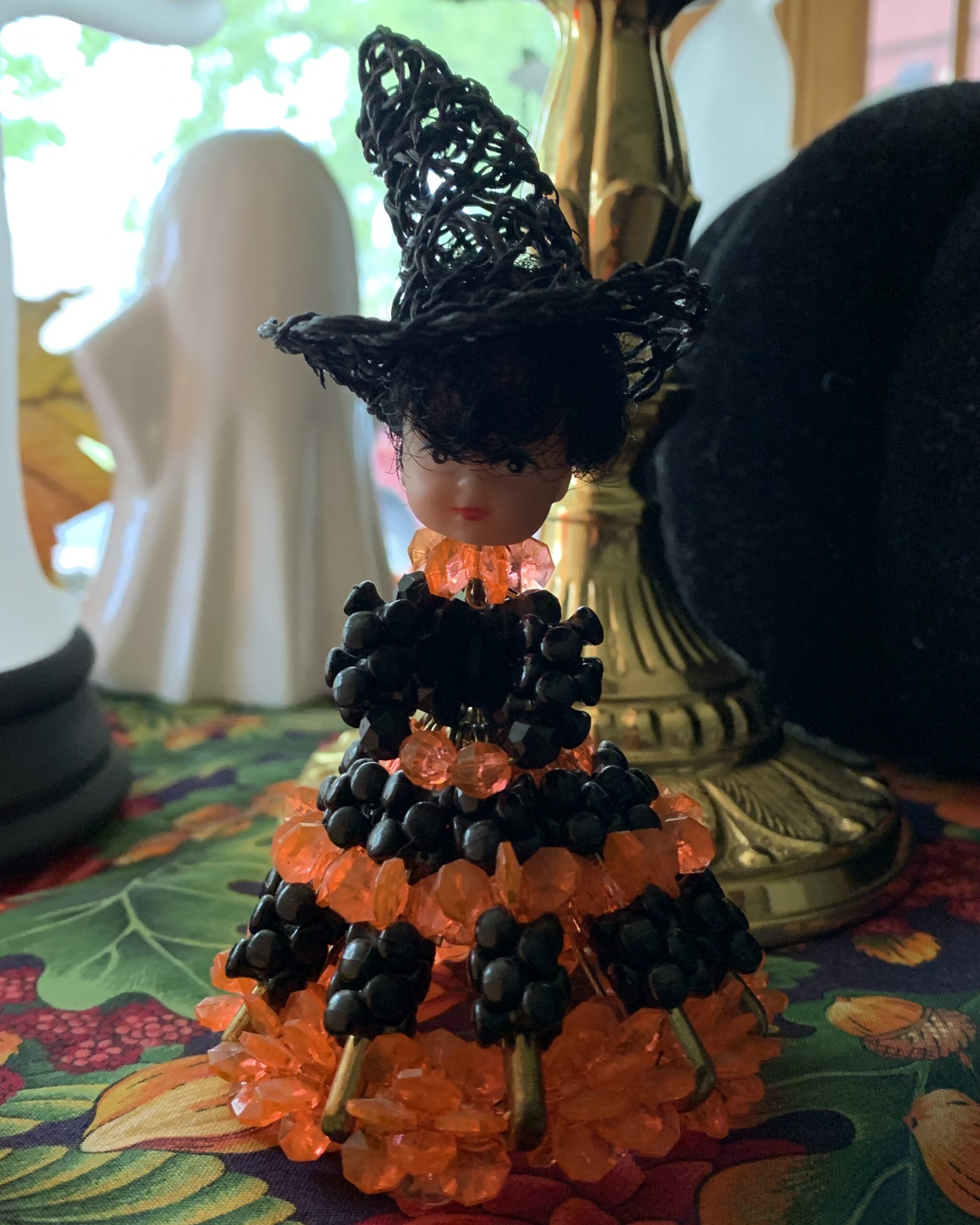 Front view of a vintage 1970s witch doll made with black and orange plastic beads, wearing a woven black witch hat.