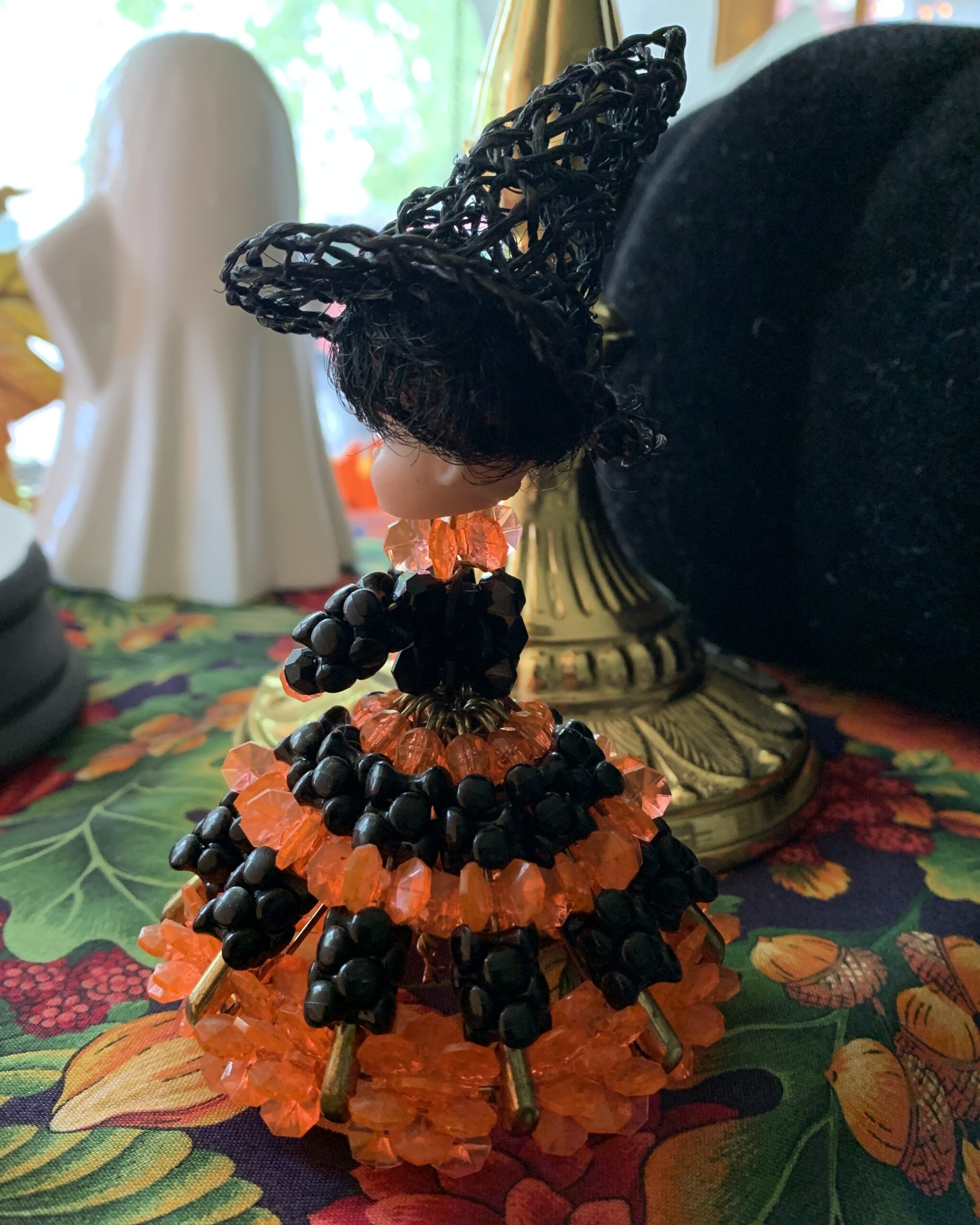 Side view of the 1970s beaded witch doll showing her layered black-and-orange beaded skirt and brass-tone wire frame.