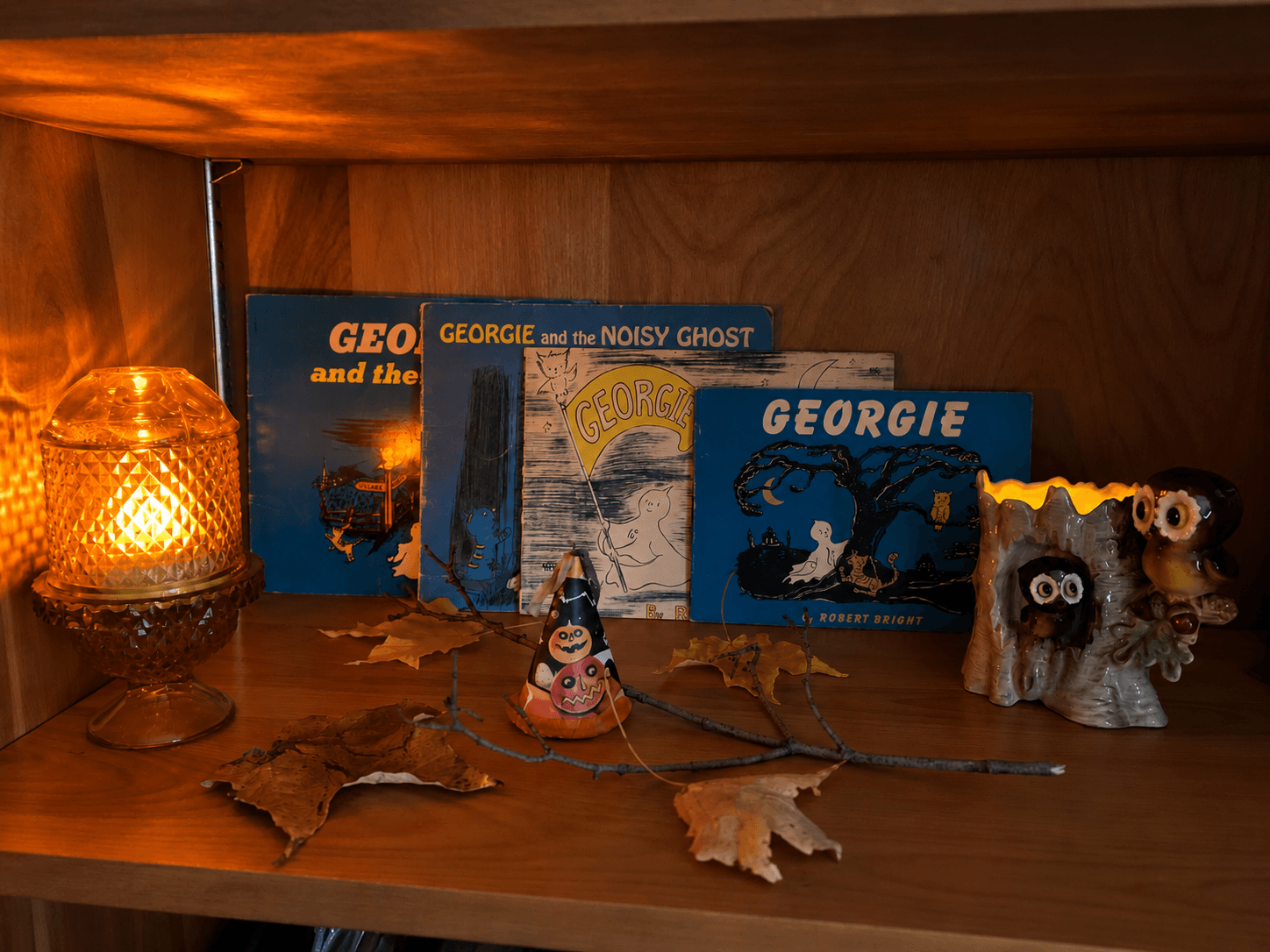 Four vintage Georgie the Ghost books by Robert Bright styled on a warm Halloween shelf with amber light, autumn leaves, and owl decor.