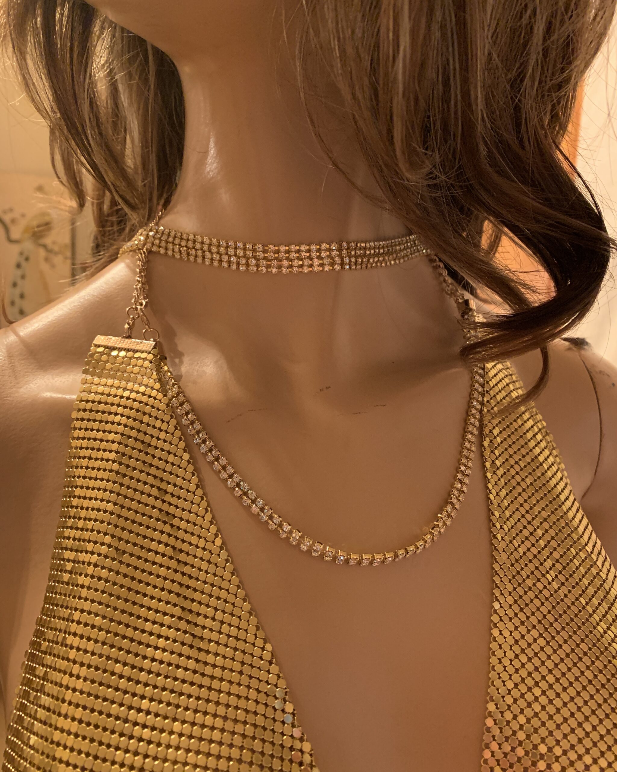 Detail of gold metal mesh and a rhinestone chain draped across the neckline.