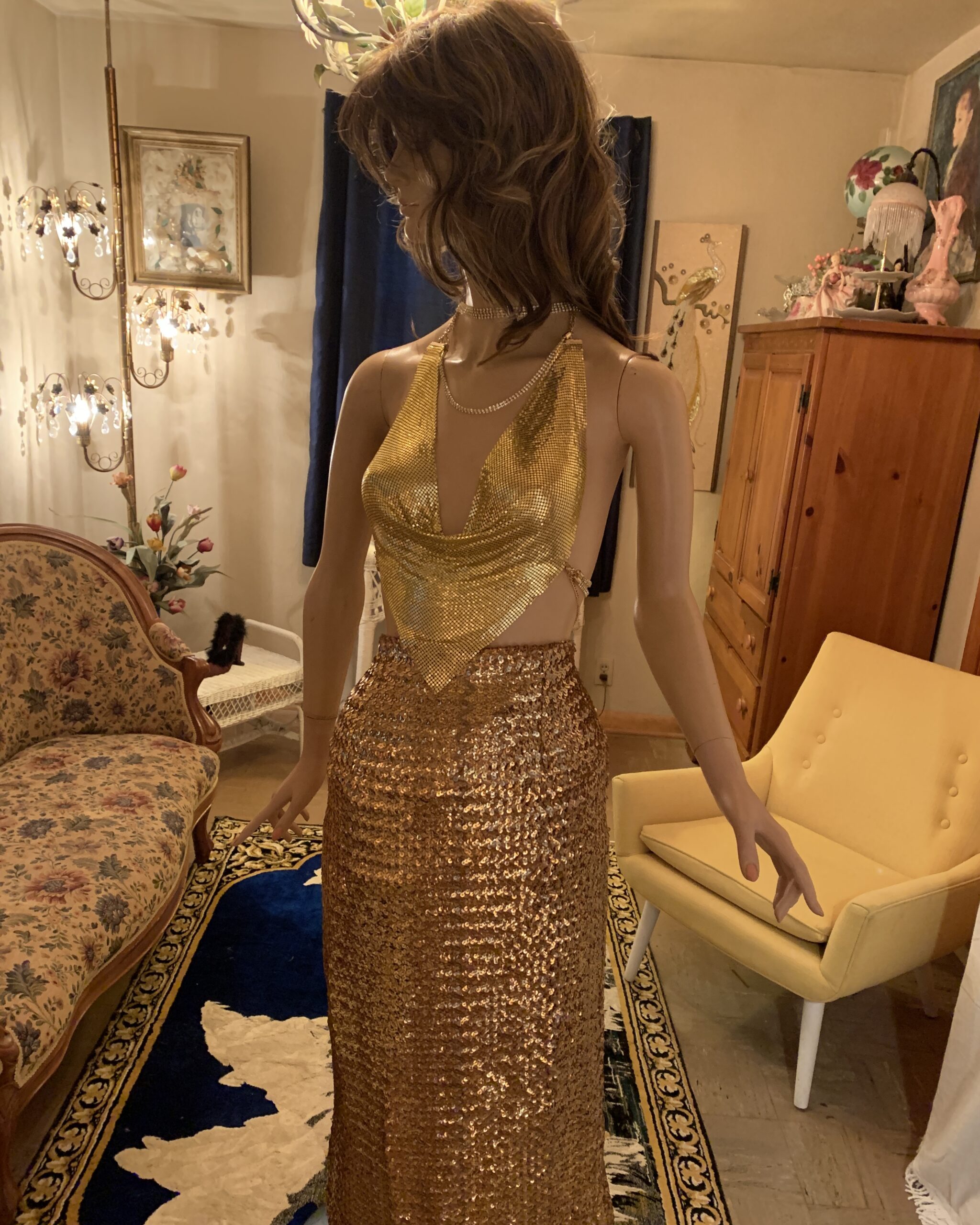 Full-length front view of a mannequin wearing a draped gold metal mesh top and gold sequined skirt.